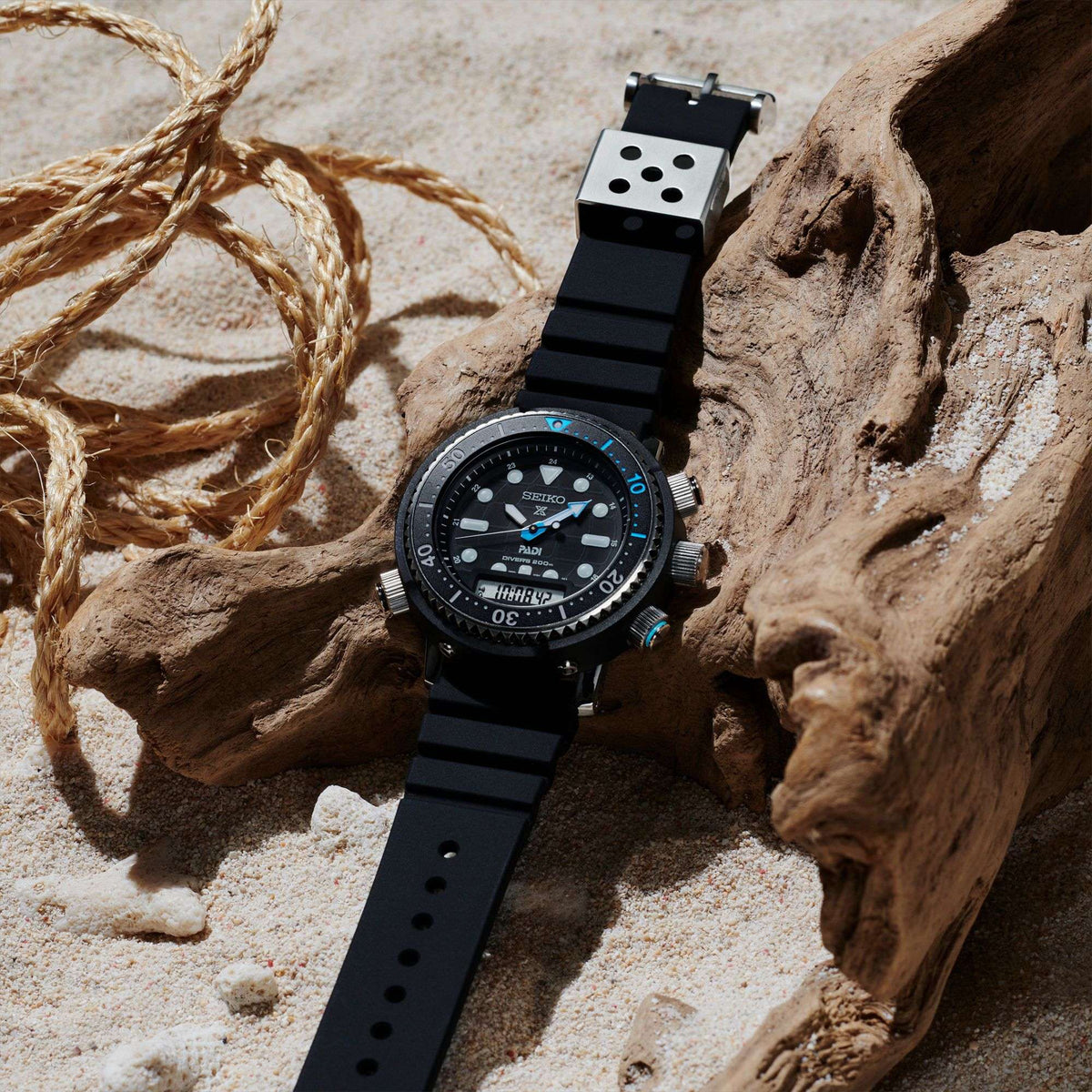 Seiko Prospex Solar ‘Arnie’ Hybrid PADI SNJ035P1F wristwatch with a detailed face on a sandy surface with driftwood