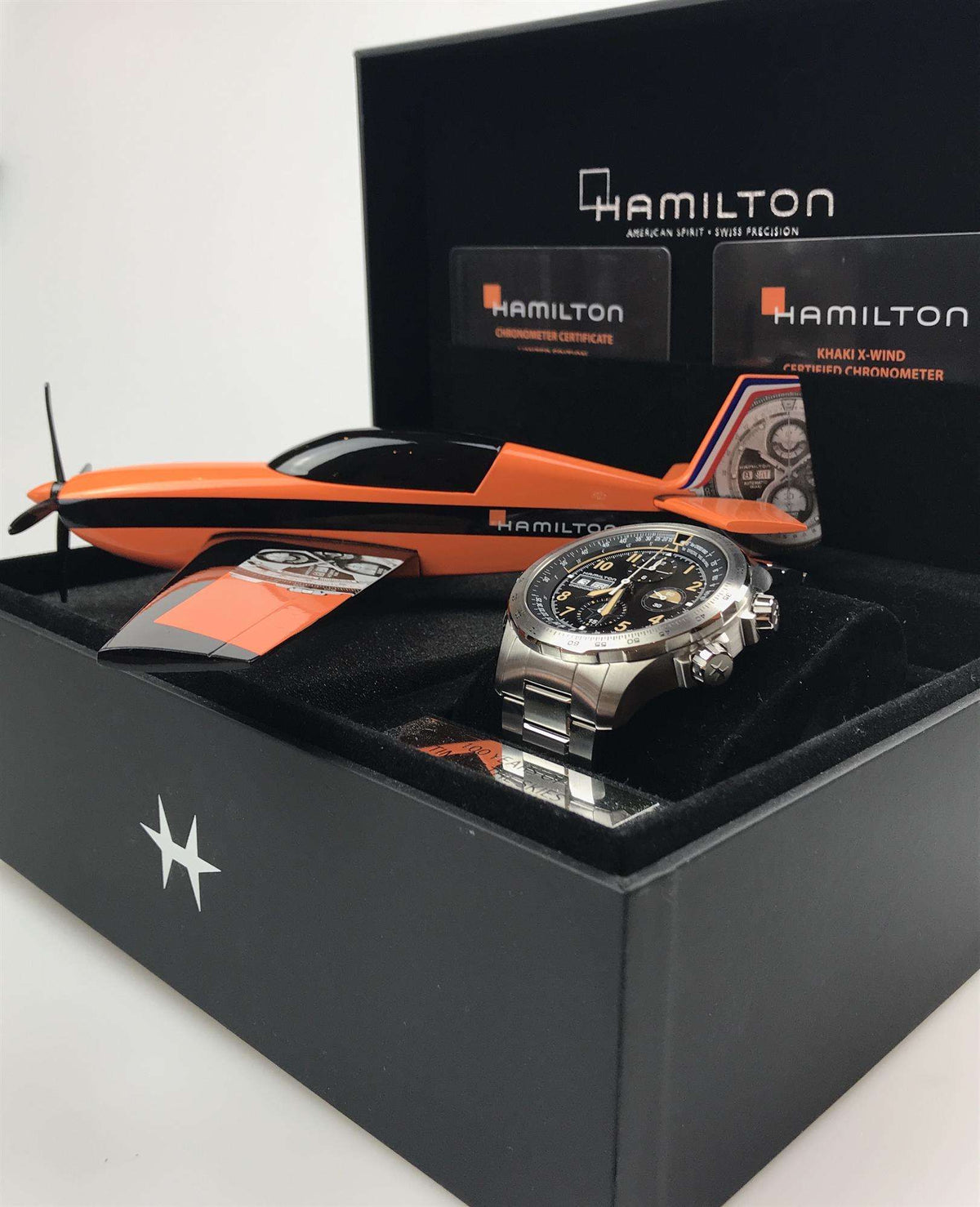 Men's steel chronograph watch on display with black dial, gold accents, and branded packaging