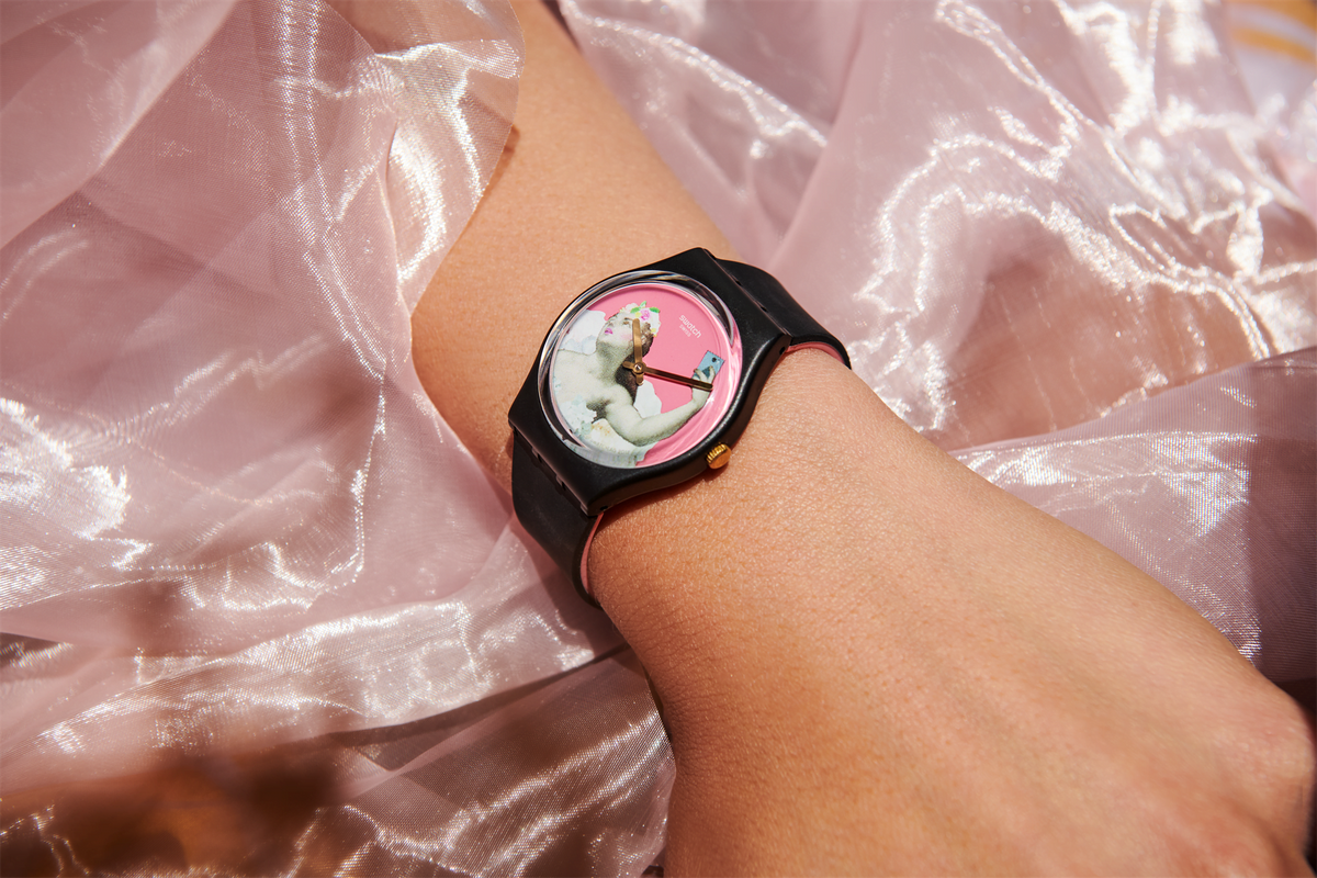 Black strap wristwatch with round pink dial on a wrist, gold-tone hands visible