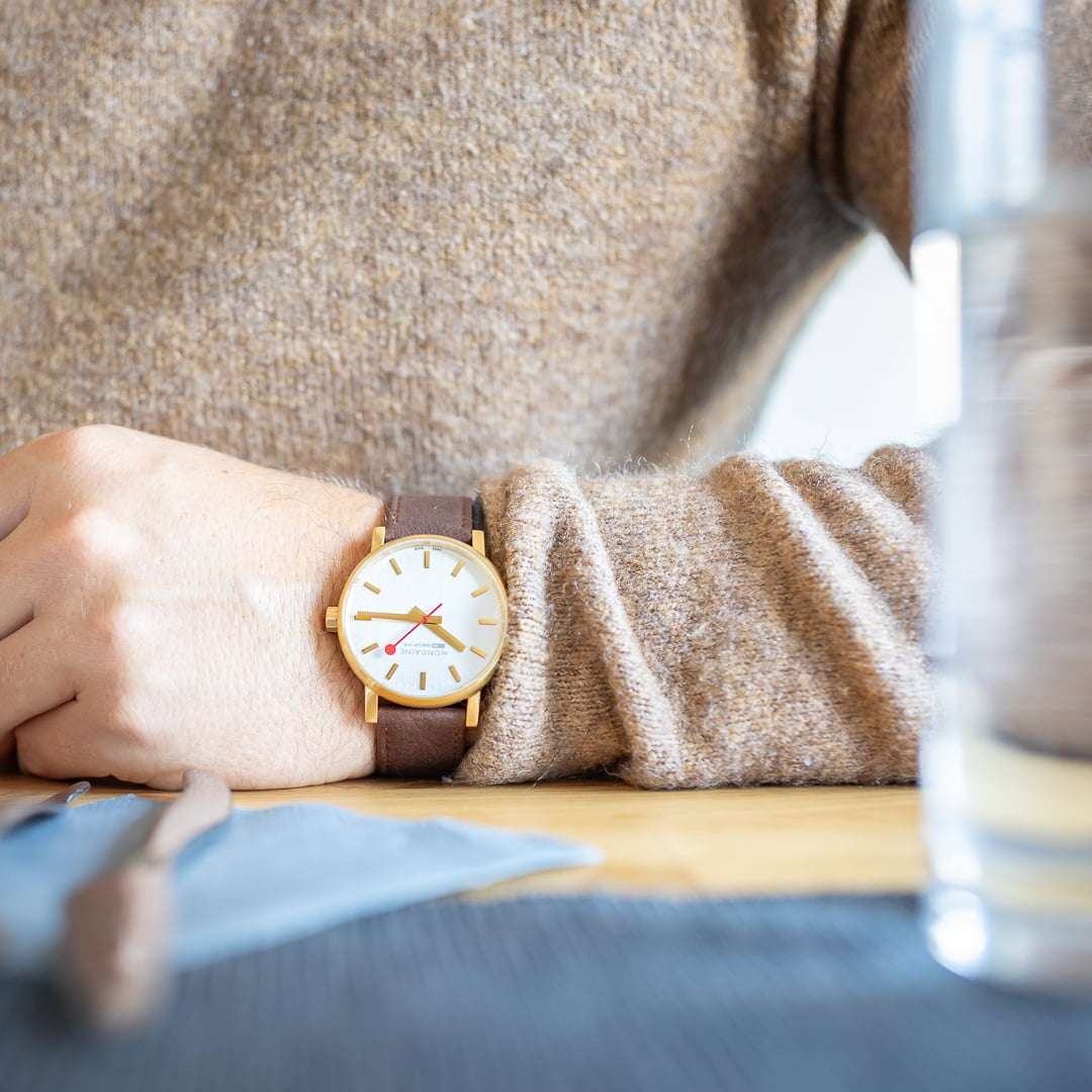 Men's gold-plated watch with brown leather strap and white dial on wrist