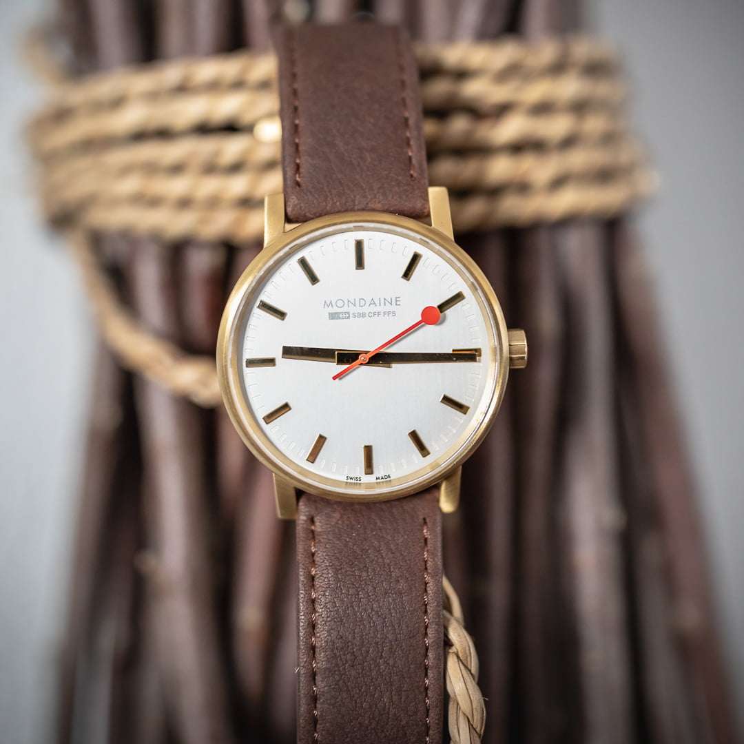 Round gold-tone watch with brown leather strap and white dial, red seconds hand