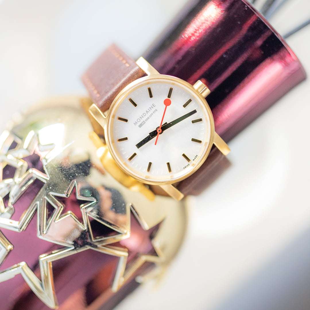 Gold-plated watch with brown leather strap and white dial, red seconds hand close-up