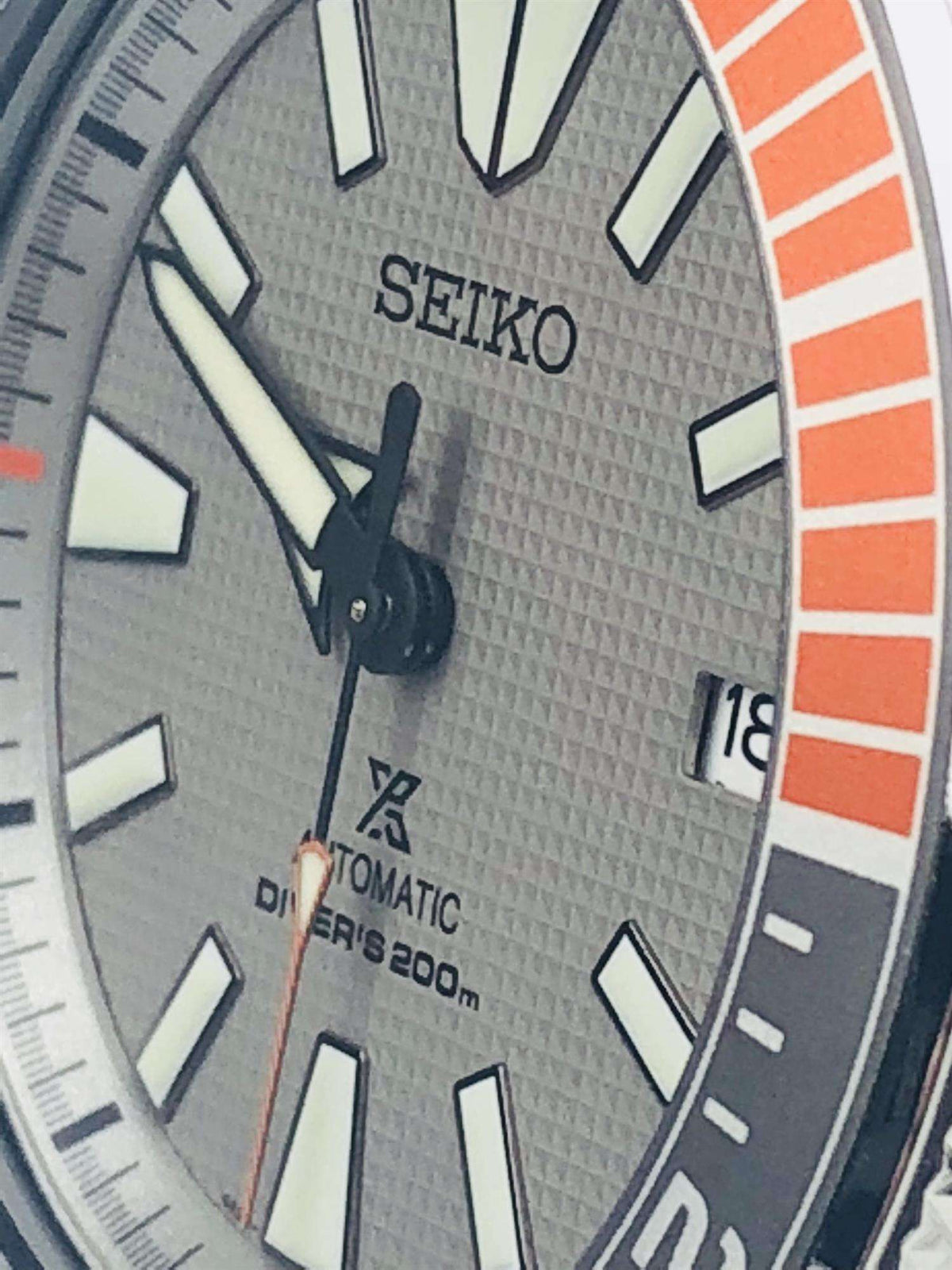 Close-up of grey textured dial with orange minute track and Seiko branding