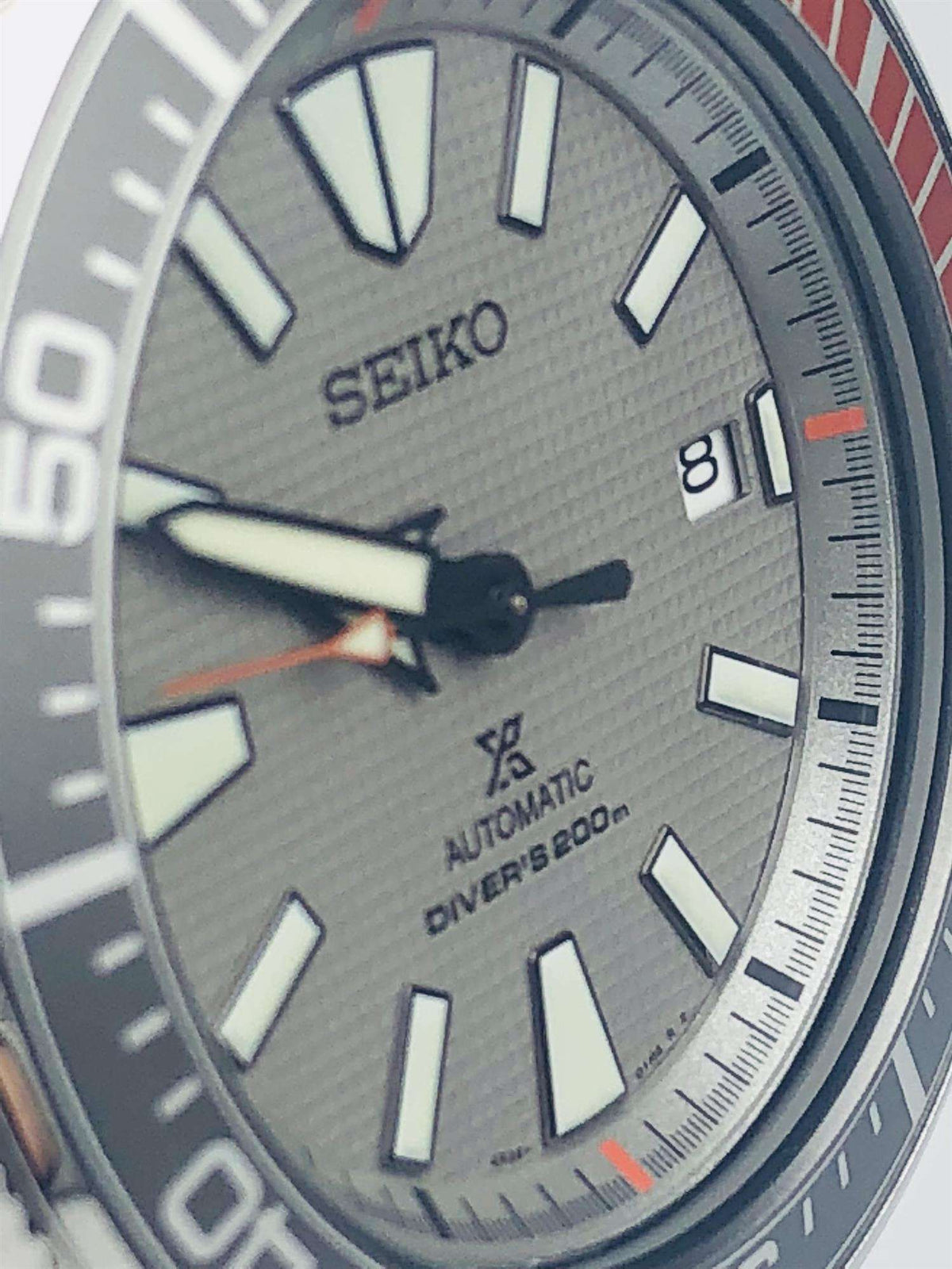 Close-up of grey dial with baton markers, orange seconds hand, and Seiko logo