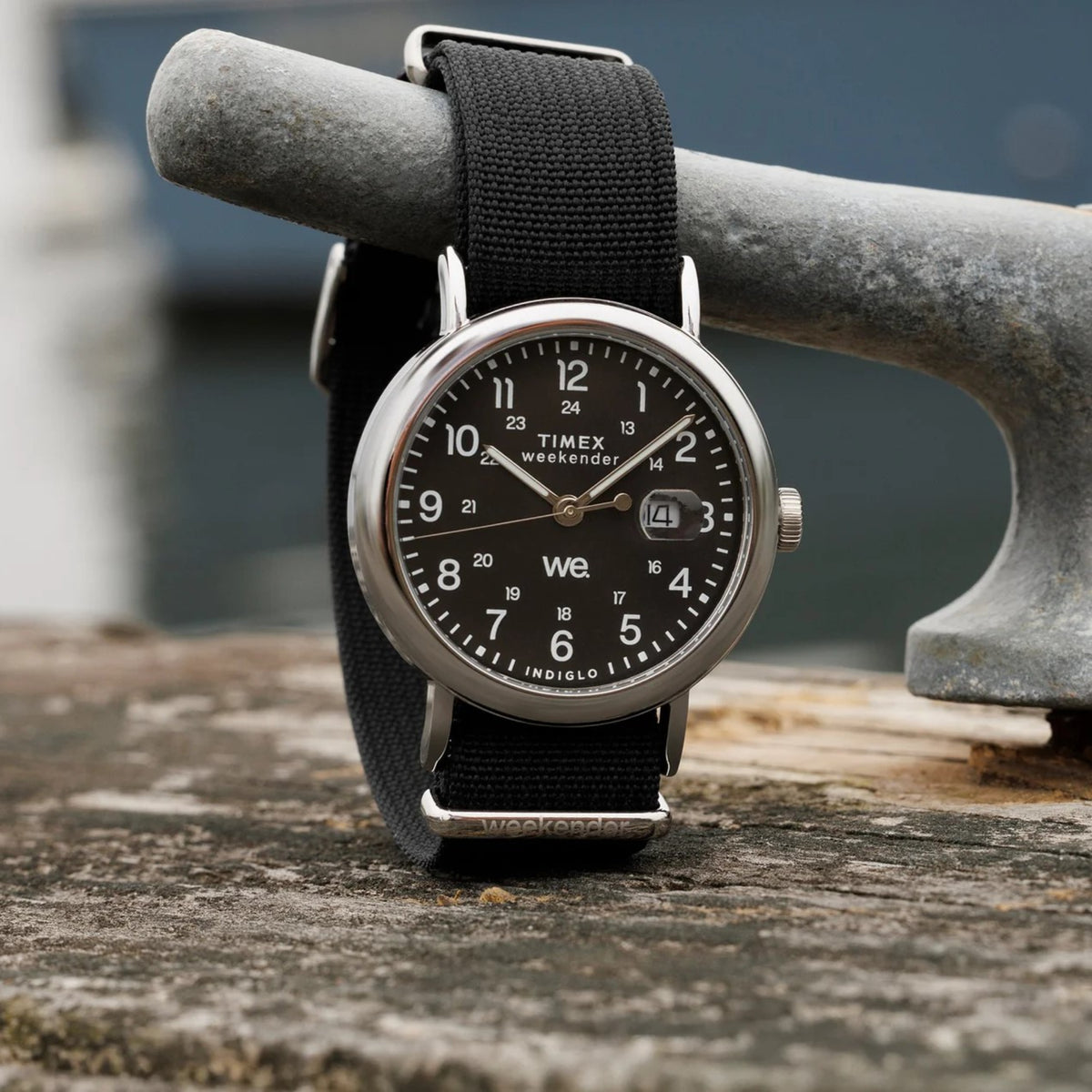 Round men’s watch with black dial and black fabric strap on a concrete ledge