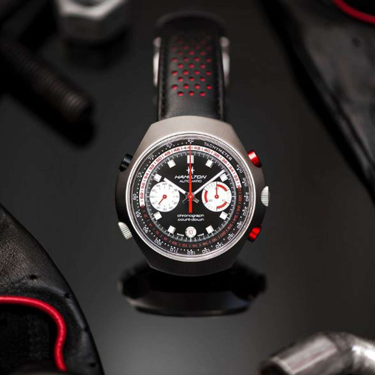 Men’s automatic chronograph watch with black dial, subdials, red details, and perforated leather strap