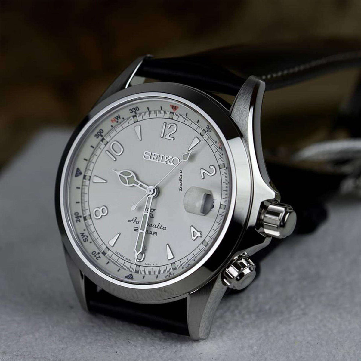 Angled view of men's automatic watch with cream dial, silver case, and black leather strap