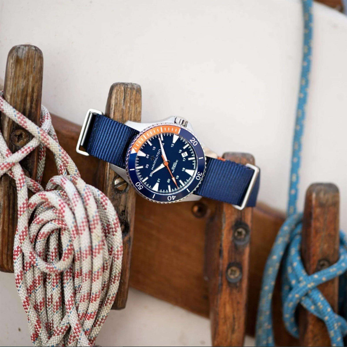 Hamilton automatic watch with blue NATO strap and dark blue dial, resting on wooden dock