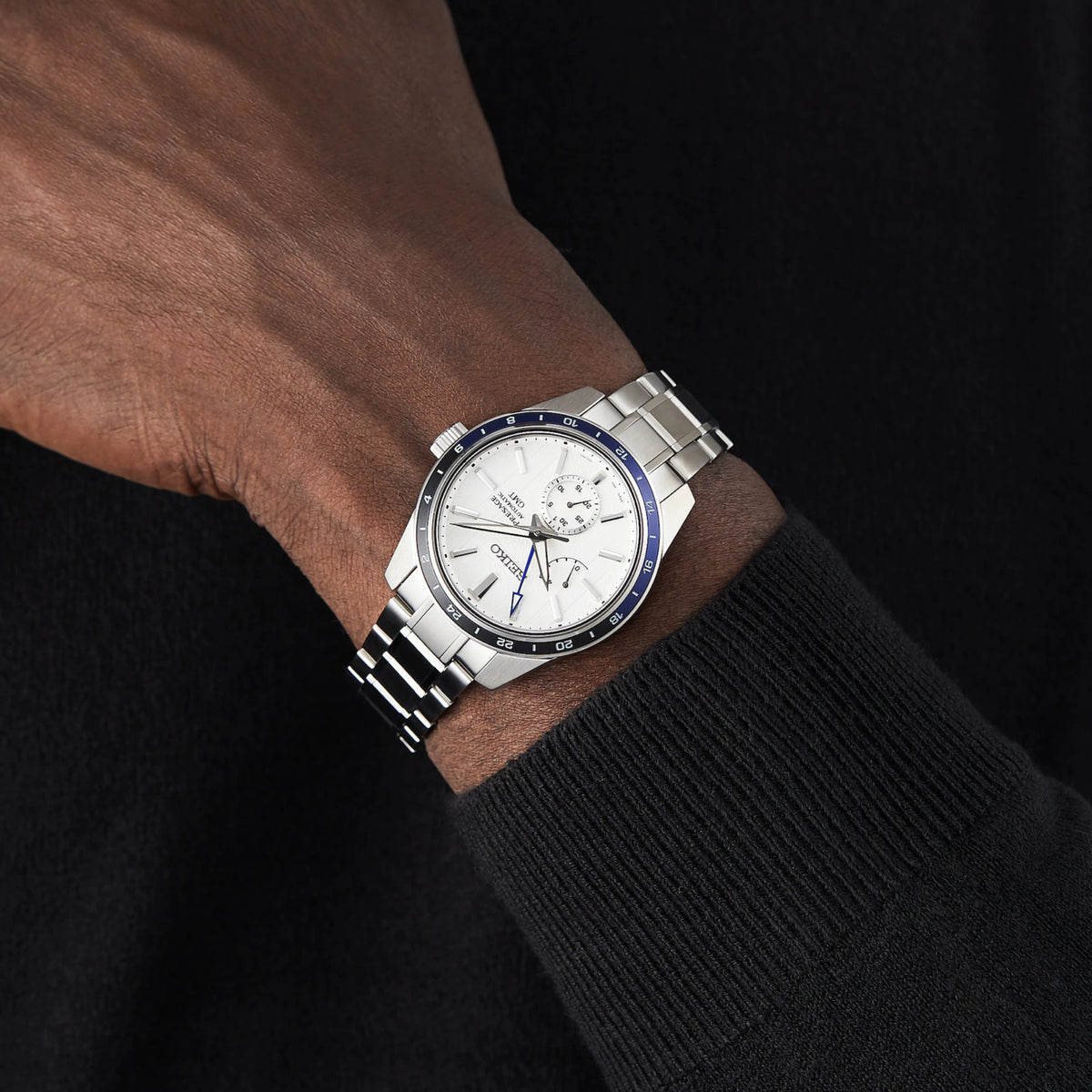 Stainless steel Seiko GMT watch on wrist with white dial and blue bezel, metal bracelet