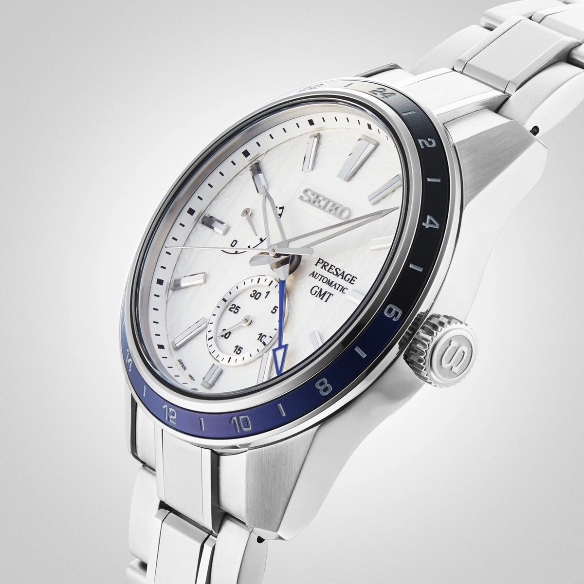 Seiko GMT wristwatch, white dial with GMT subdial, blue bezel, stainless bracelet at angle