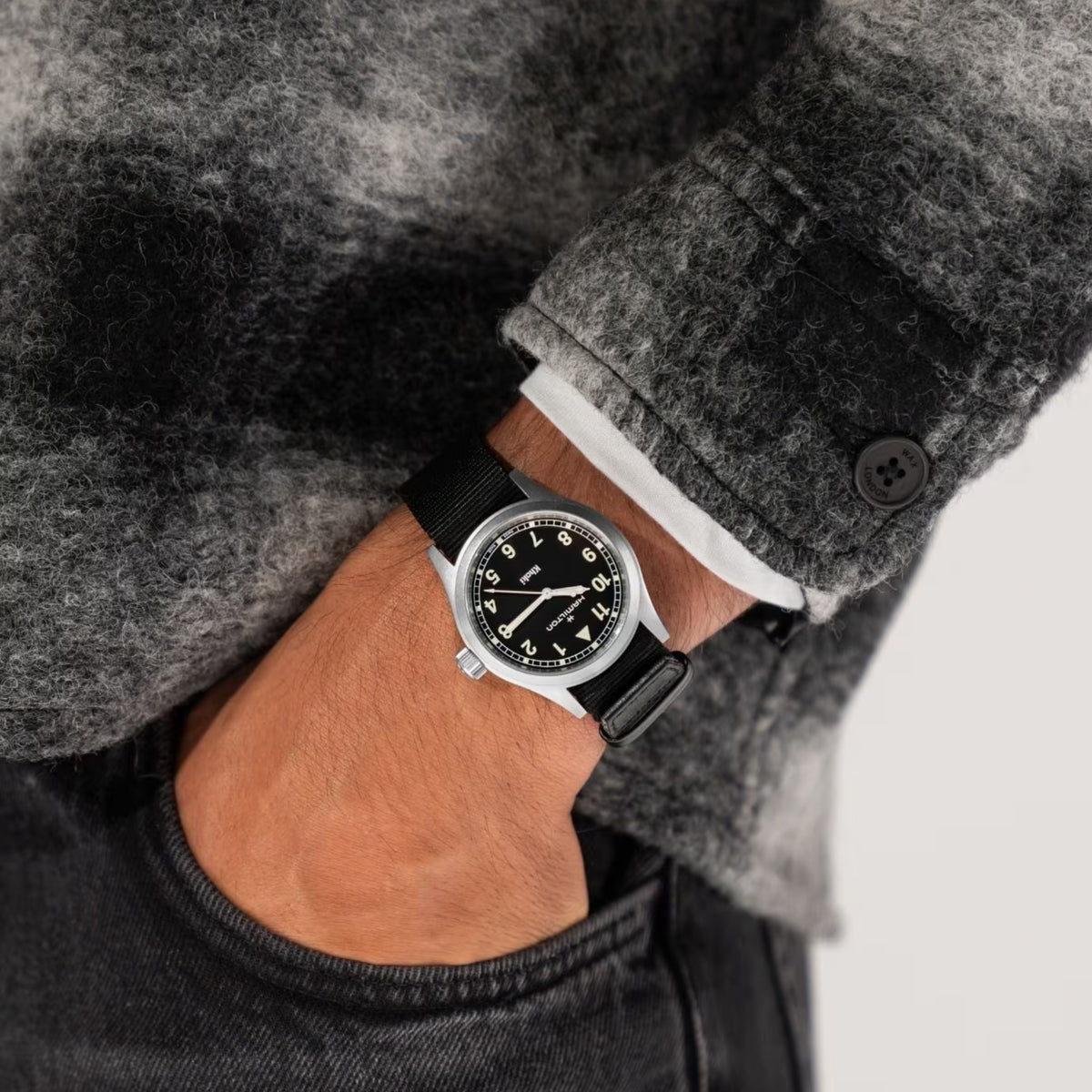 Hamilton Khaki Field H69401430 quartz watch wrist shot styled with grey patterned jacket showing black dial and black fabric band
