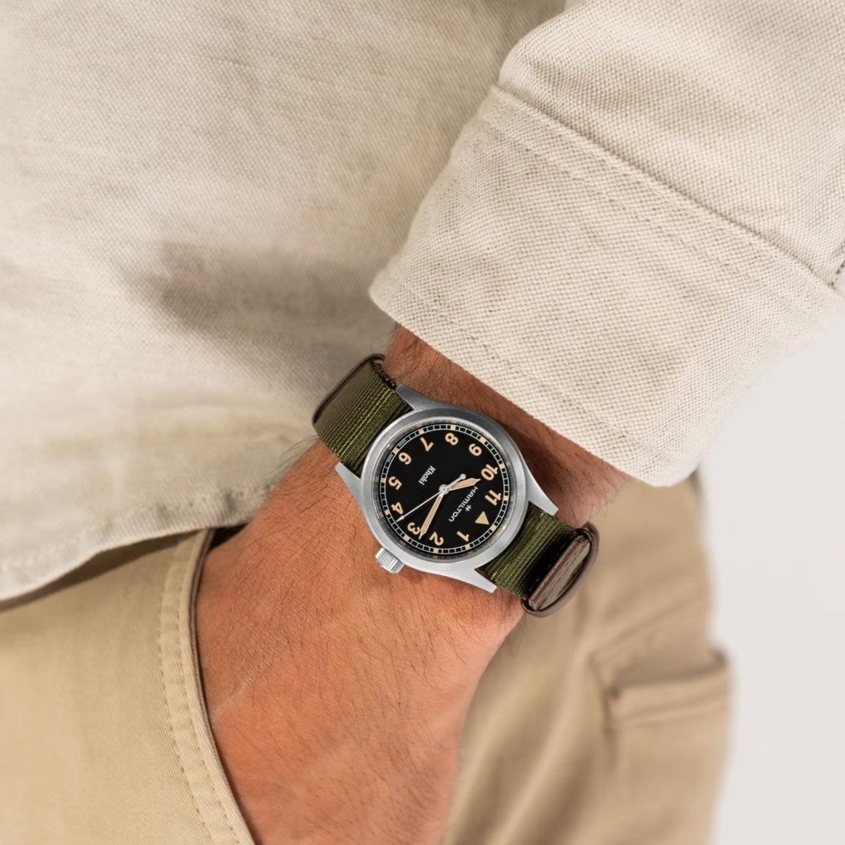 Hamilton Khaki Field H69401930 quartz watch wrist shot styled with cream linen shirt showing black dial and green fabric band