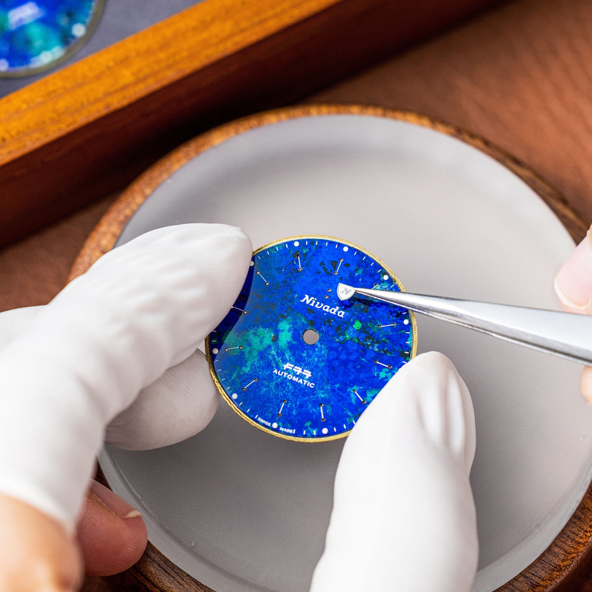 Nivada Grenchen F77 68056A77 close-up view of watchmaker fitting logo onto azurite dial