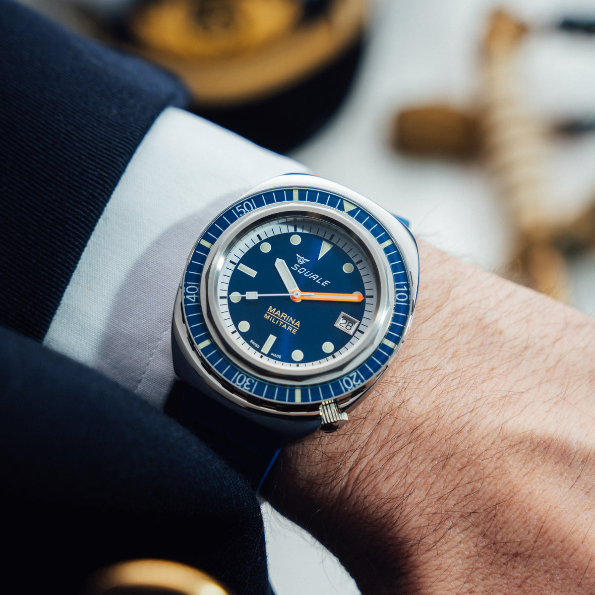 Men's automatic watch on wrist with blue rubber strap, navy dial, orange hands, date window