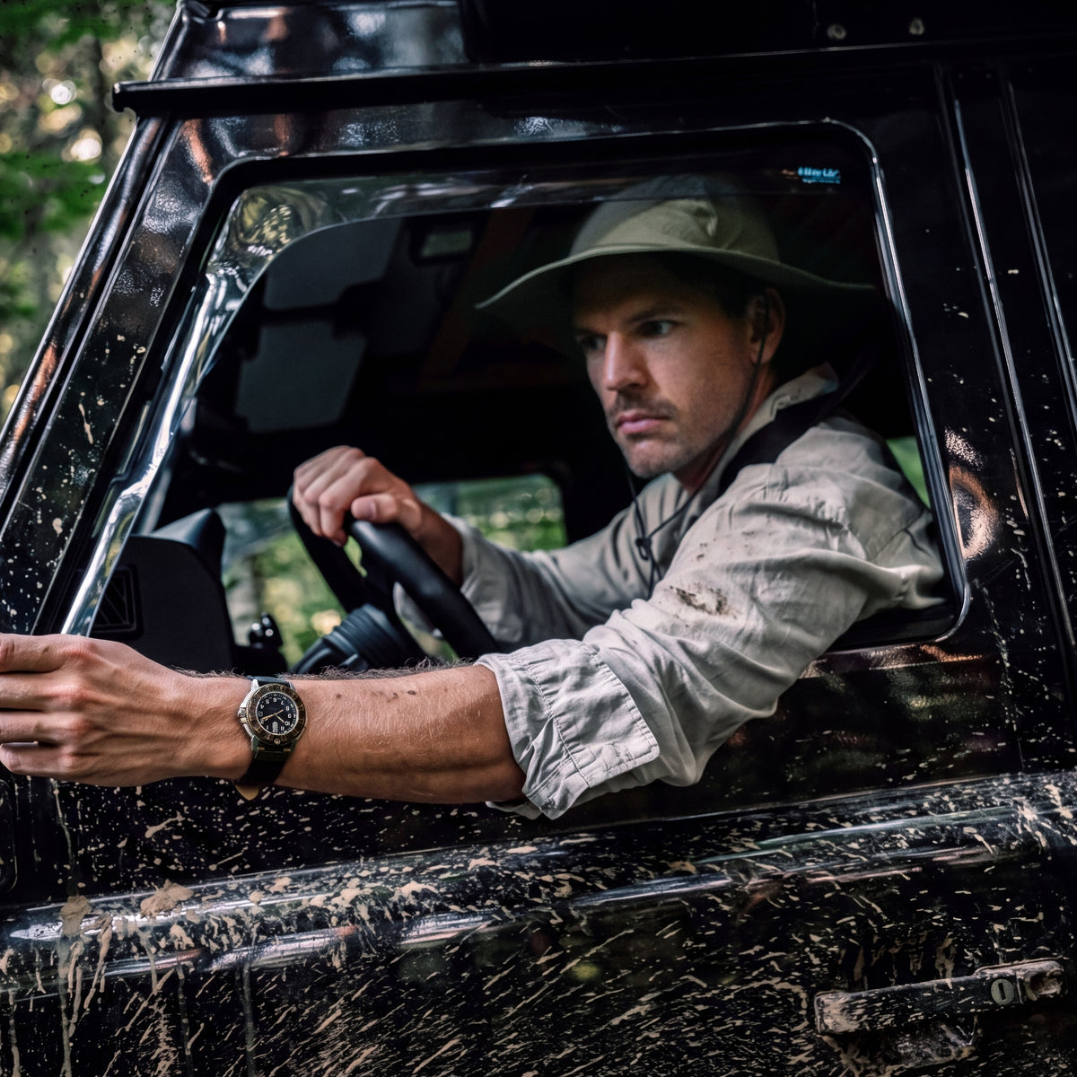 A man wearing a Luminox Adventure Watch drives a muddy off-road vehicle during an outdoor excursion
