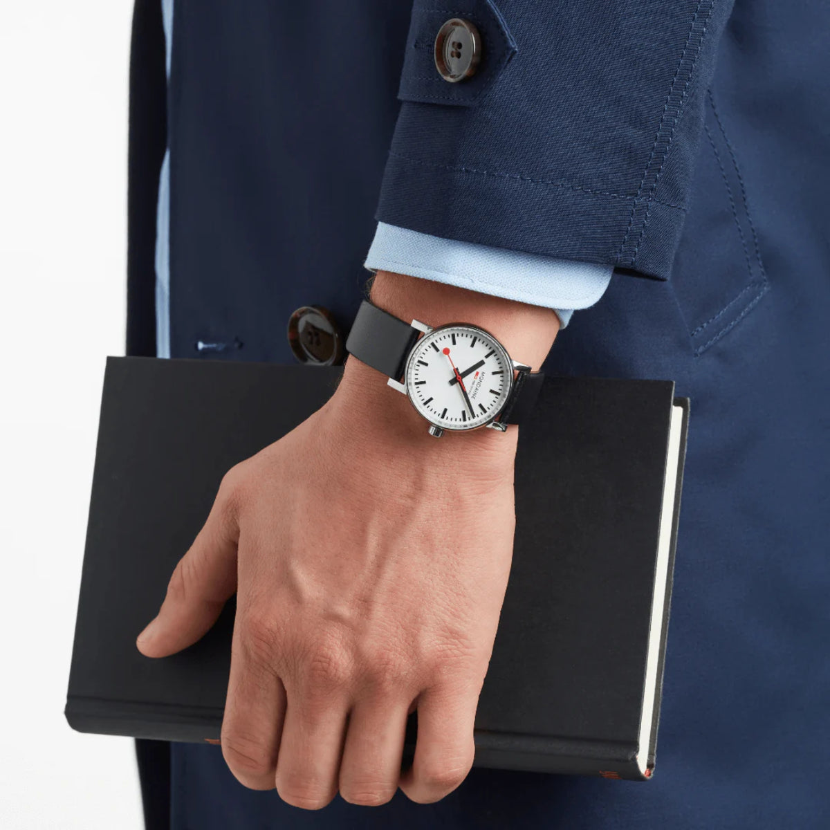 Mondaine Evo2 MSE.35110.LBV classic Swiss Railways watch worn on the wrist, paired with a navy trench coat and light blue shirt