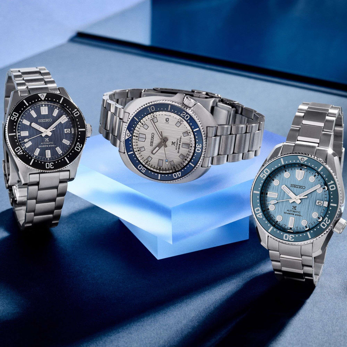 Three stainless steel diver watches with dark, blue, and white dials