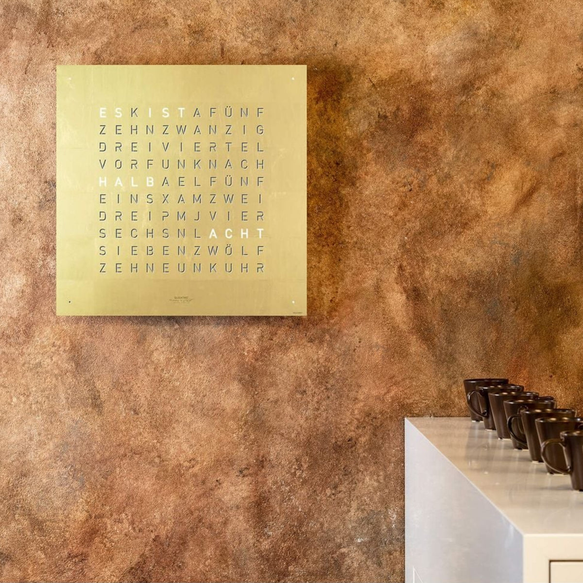 Gold English wall clock face with illuminated letter grid and raised wording