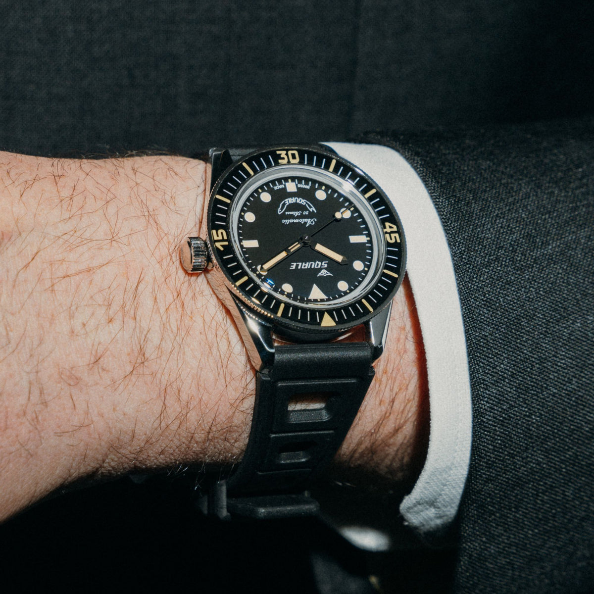 Men's black dial dive watch with black rubber strap on wrist, side angle