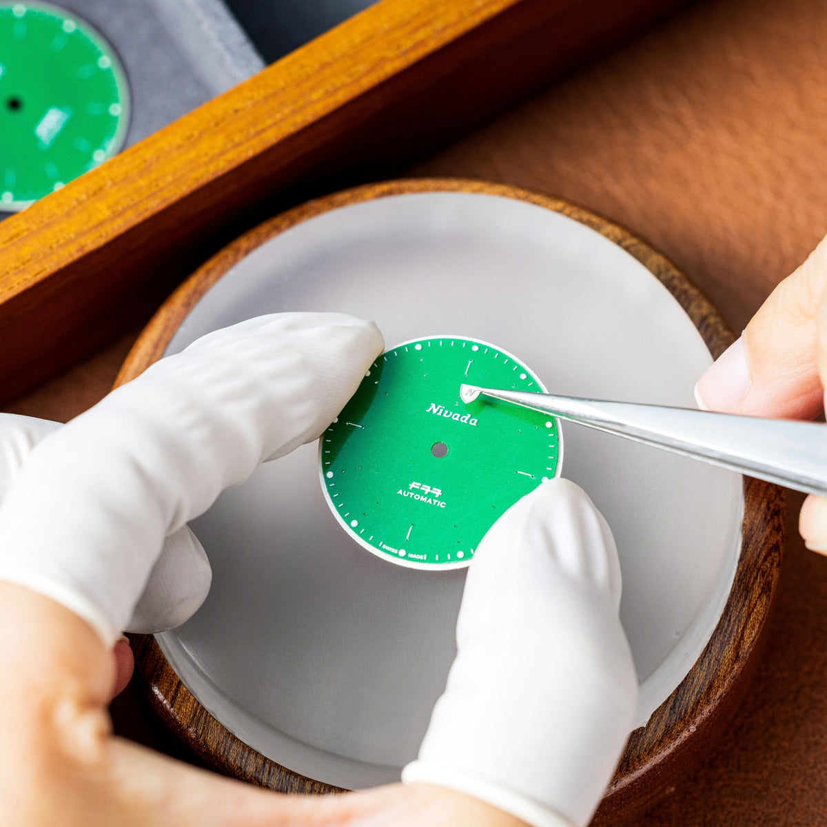 Nivada Grenchen F77 68055A77 watchmaker positioning logo onto jade dial with precision tweezers
