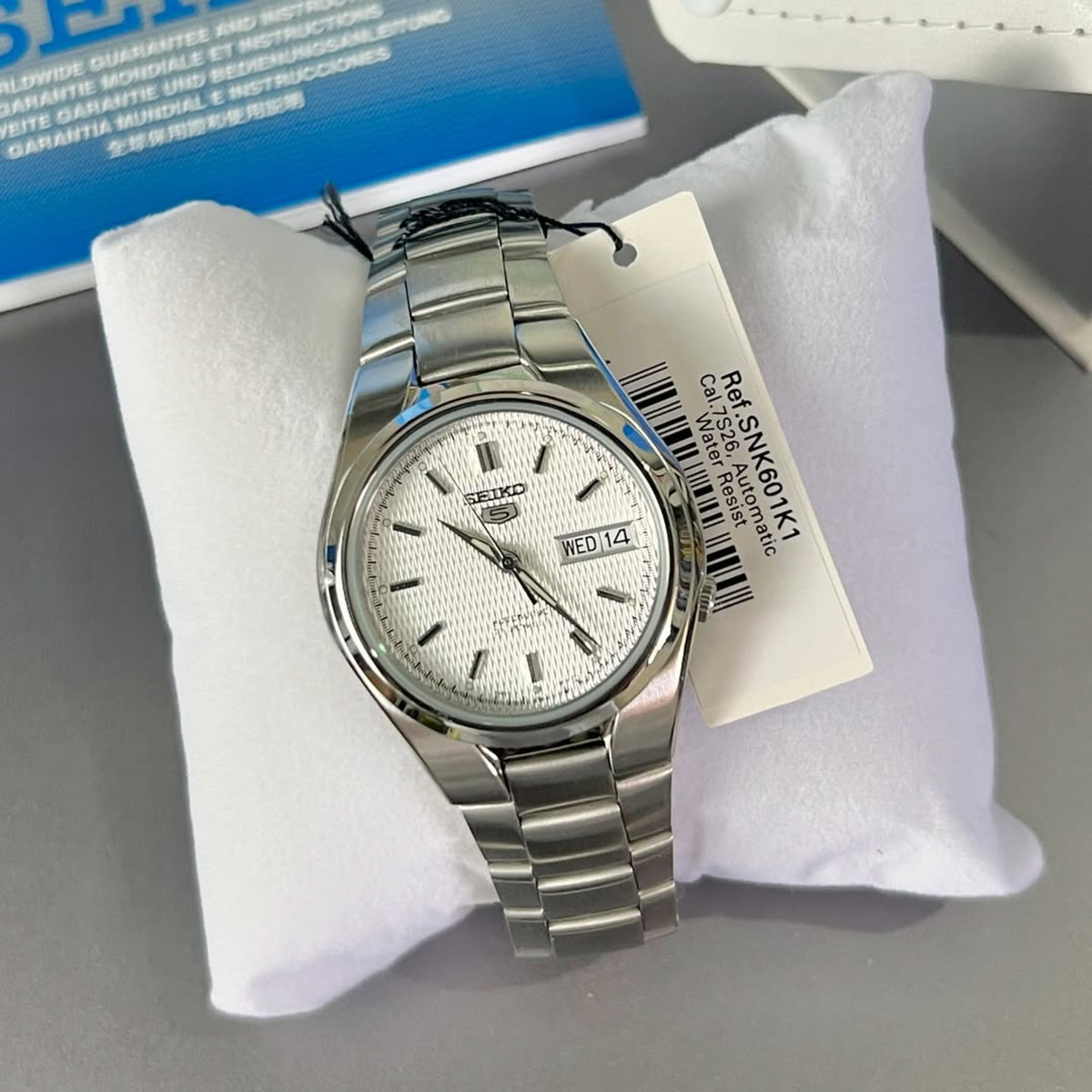 Seiko 5 SNK601K1 mens automatic timepiece resting on a display cushion with a product tag