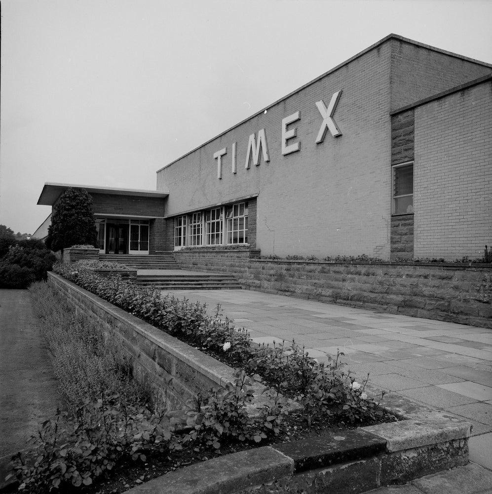Vintage black and white photograph of mid-century Timex watch factory entrance with stone landscaping