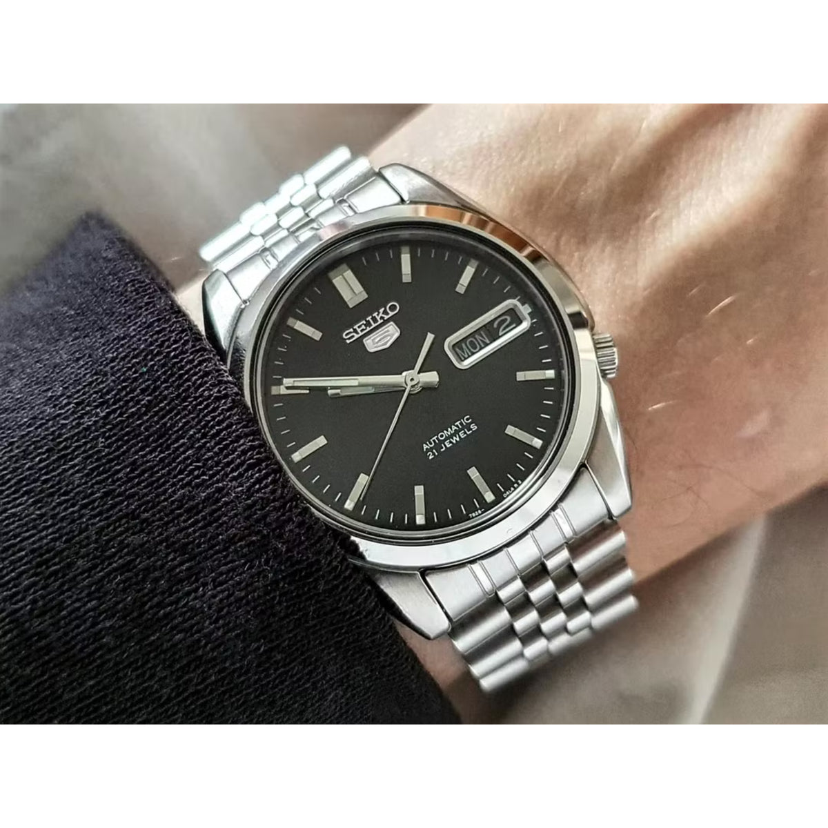 Men's stainless-steel watch on wrist with black dial, markers, and date window