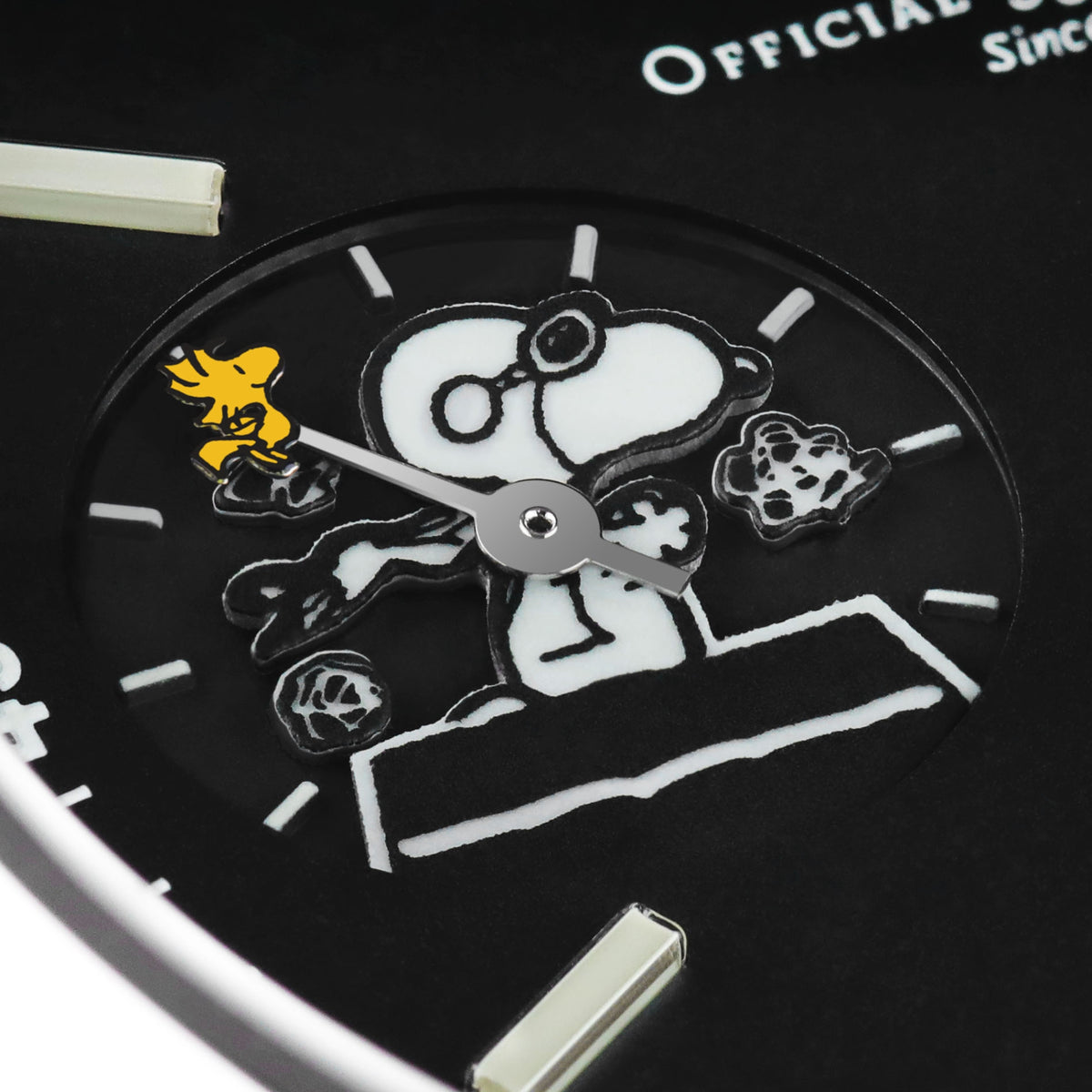 Black dial close-up with Snoopy figure and silver hands on a men's wristwatch.