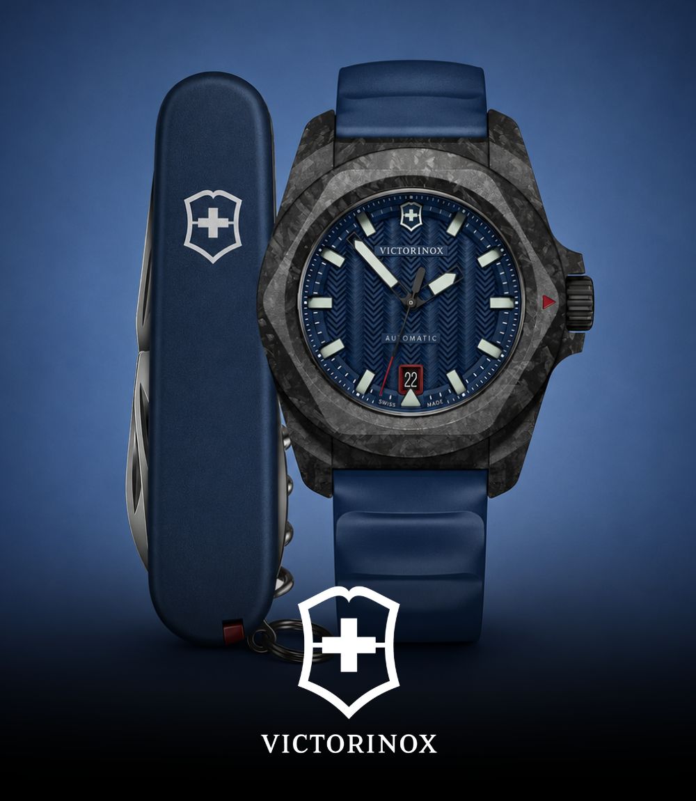 Victorinox automatic watch featuring a dark forged carbon case, blue textured dial, and blue rubber strap, displayed next to a matching blue Swiss Army knife, featuring the Victorinox logo at the bottom