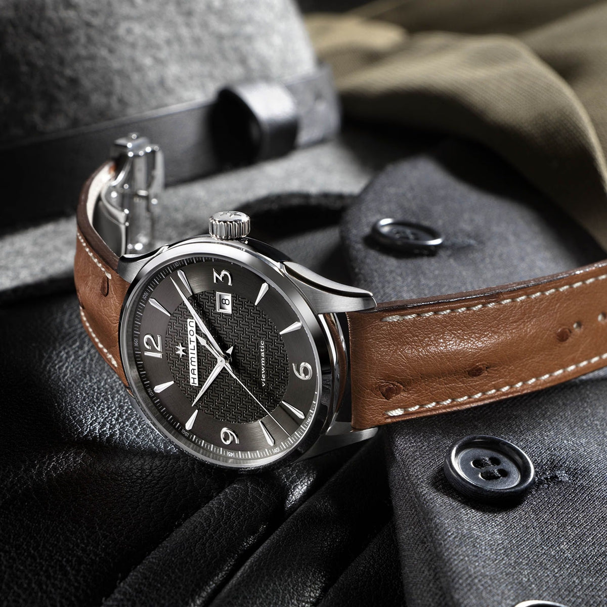 Men's automatic watch on dark fabric: grey dial, silver case, tan leather strap