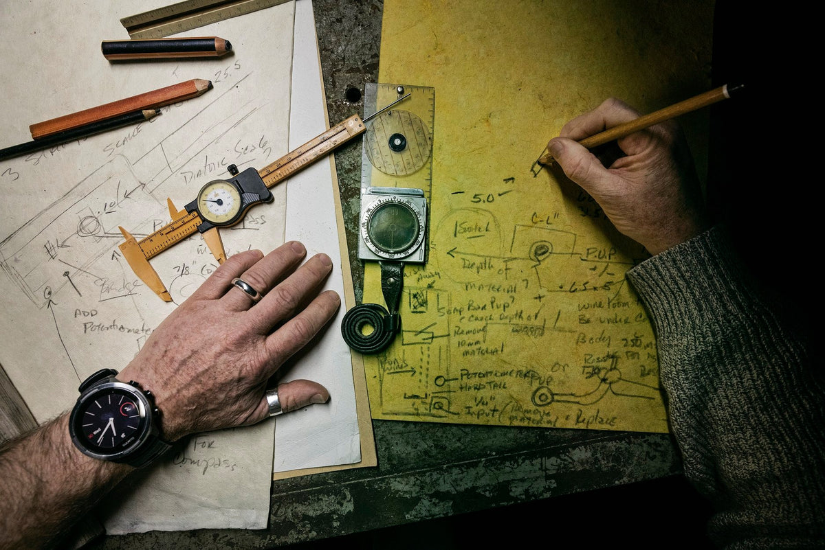 Handmade blueprint drafting table featuring vintage Suunto compass and modern Suunto GPS smartwatch