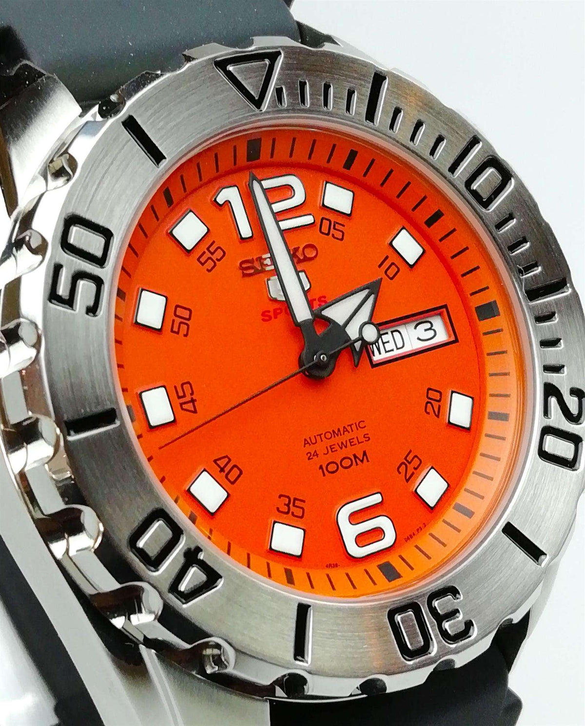 Orange dial close-up with baton markers and day-date window on stainless case