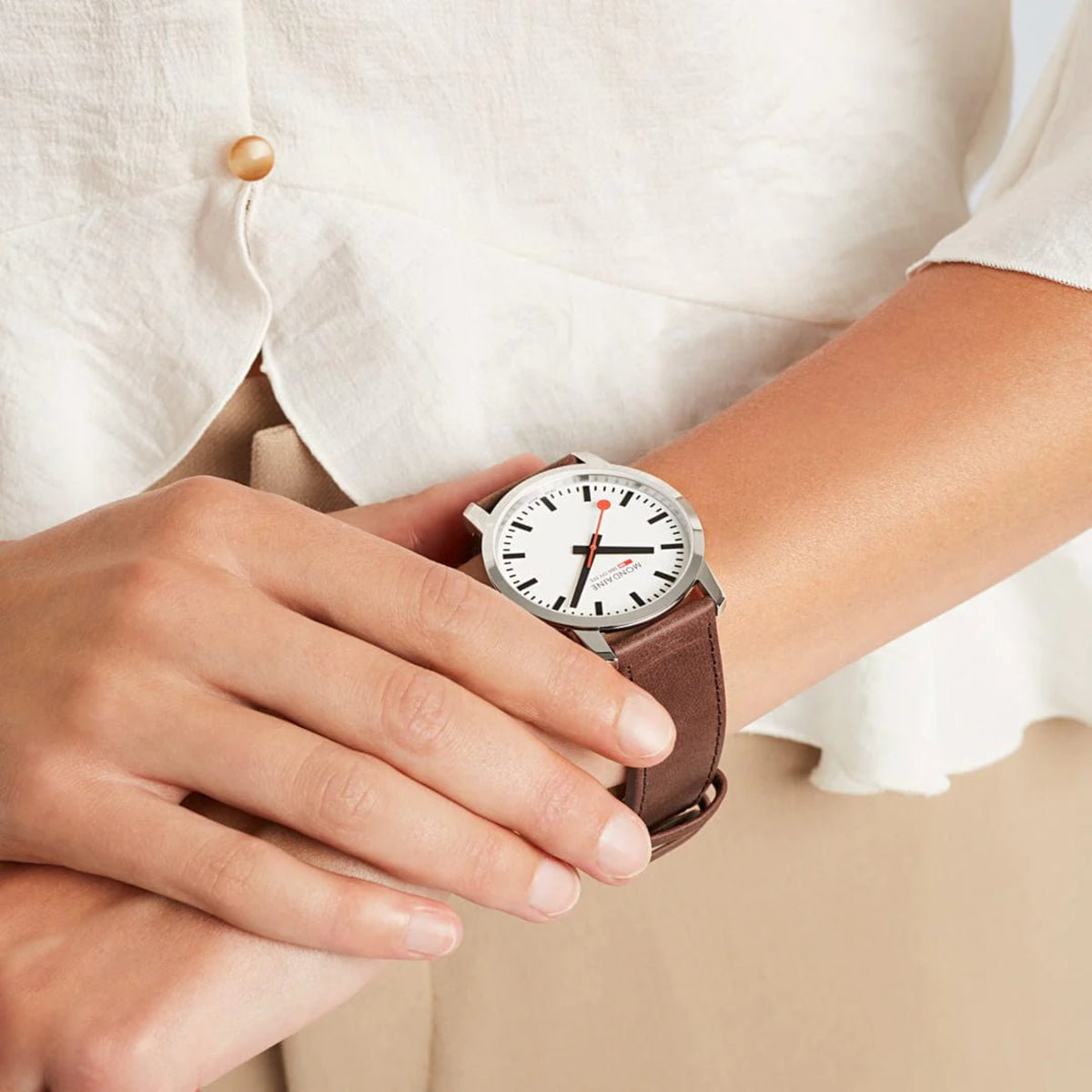 Men's wristwatch on wrist with white dial, silver case, and brown leather strap