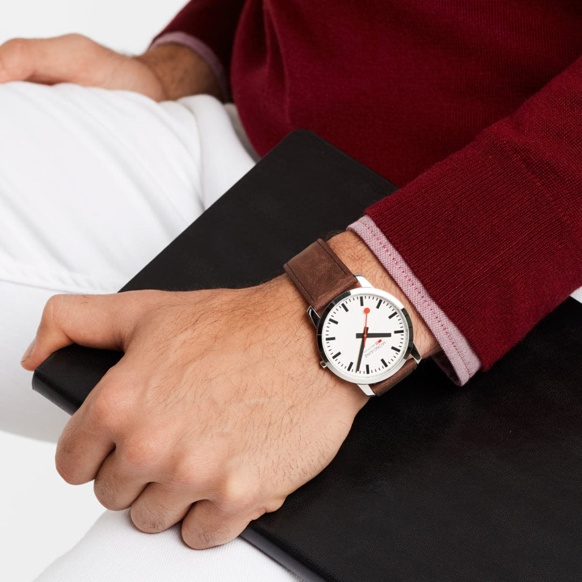 Men's wristwatch on wrist with white dial, red seconds hand, and brown leather strap