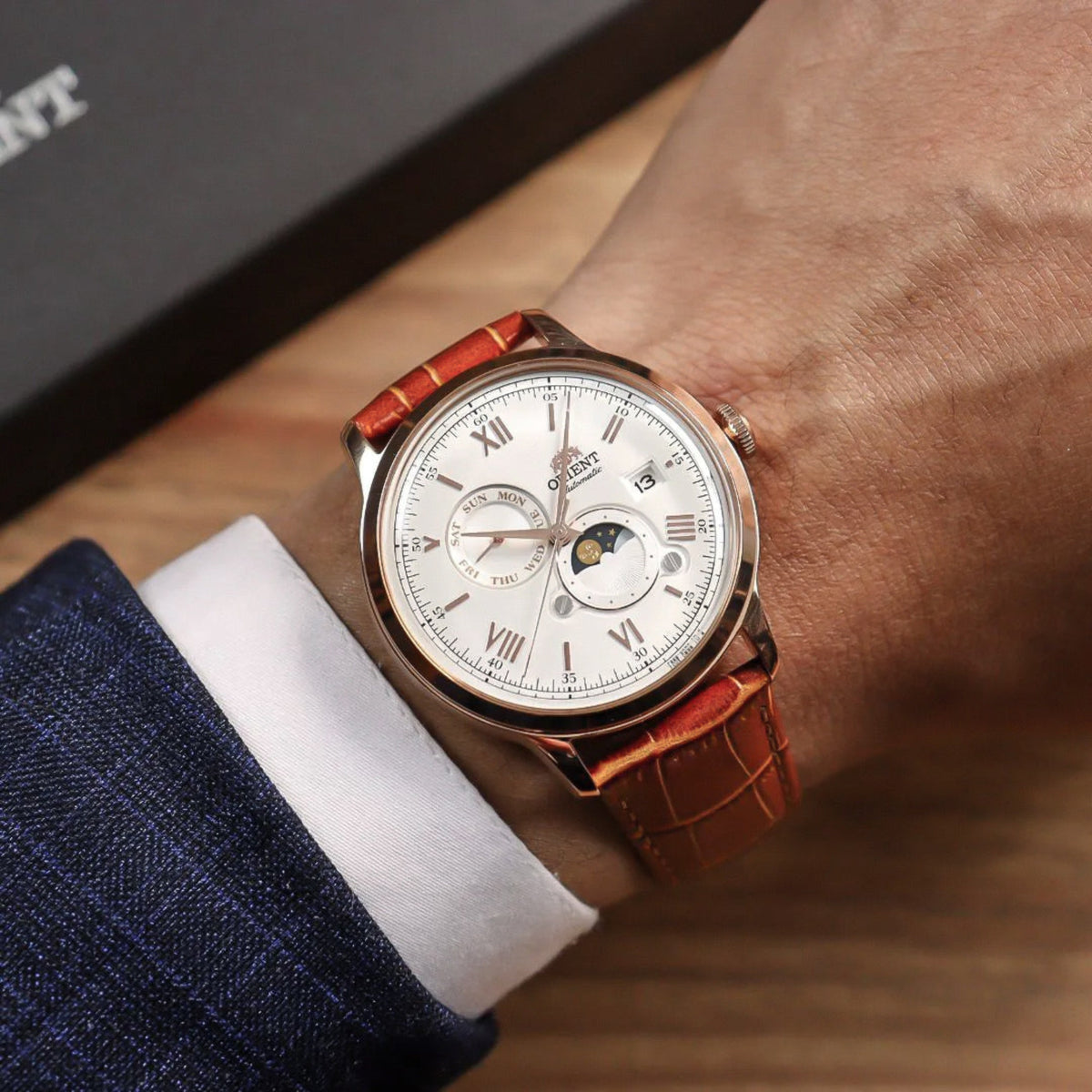 Orient Bambino Sun & Moon RA-AK0801S30B watch on wrist with silver dial, Roman numerals, moon-phase subdial, and brown leather strap