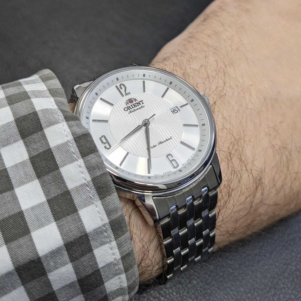 Stainless steel automatic watch with white dial on wrist, metal link bracelet