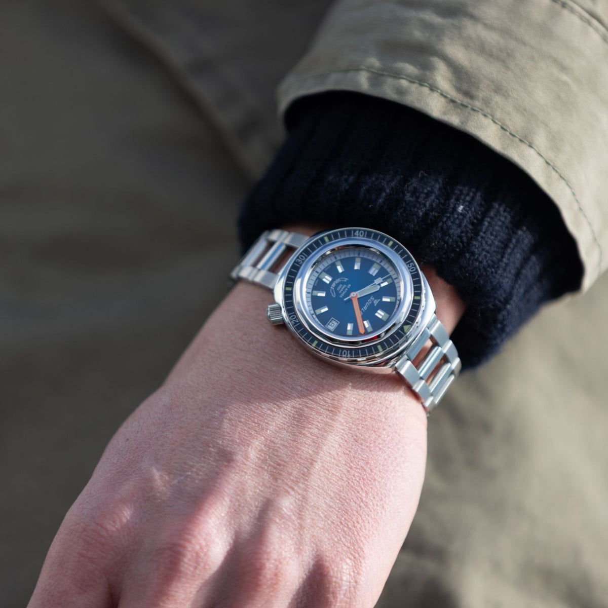 Men's blue dial watch on wrist with stainless steel bracelet and black bezel