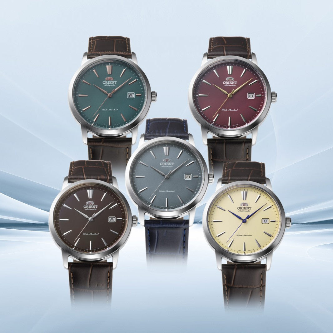 Five Orient classic dress watches displaying colored dials in green, red, brown, grey, and cream with leather straps
