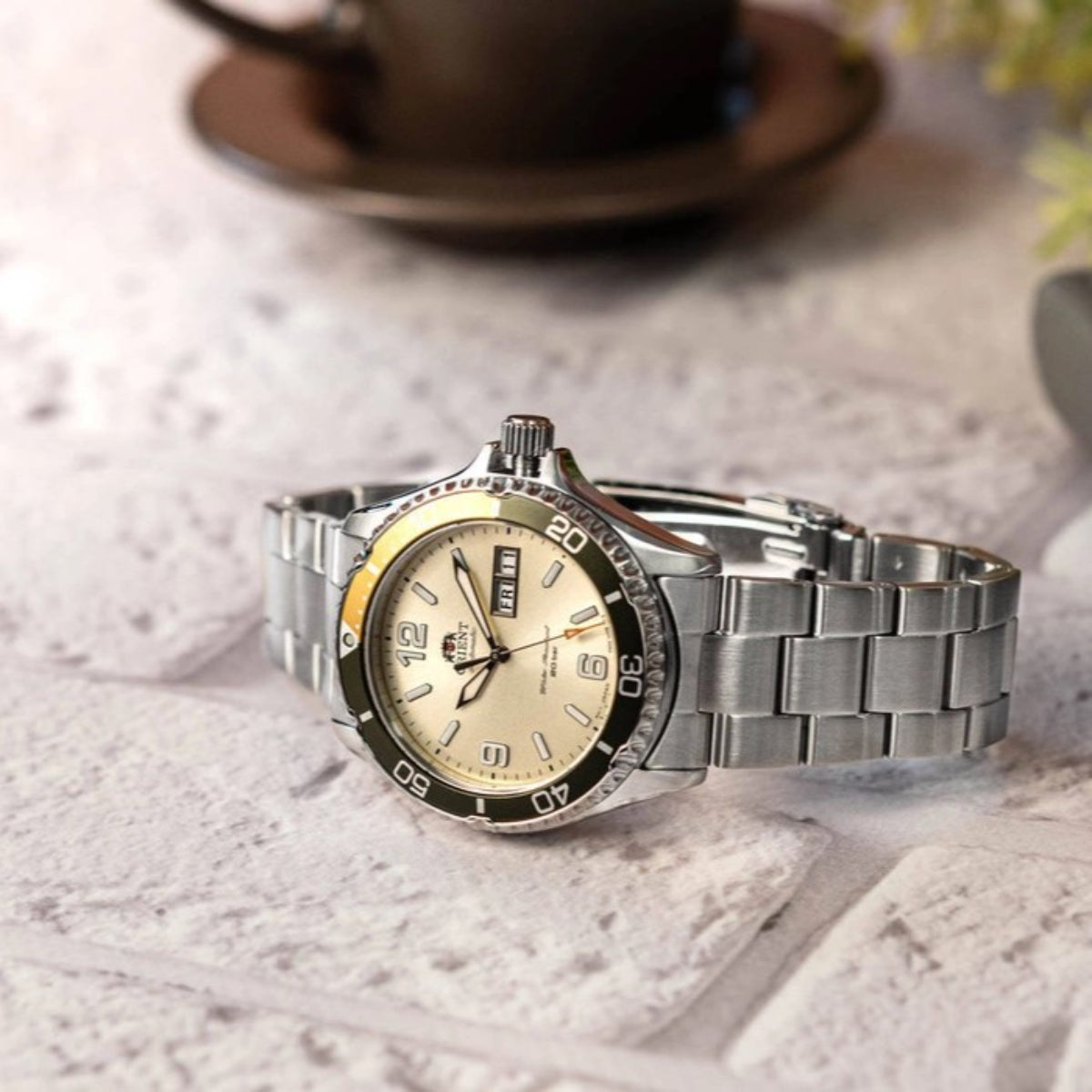 Men's automatic steel watch on wrist with ivory dial, yellow accents, and metal bracelet