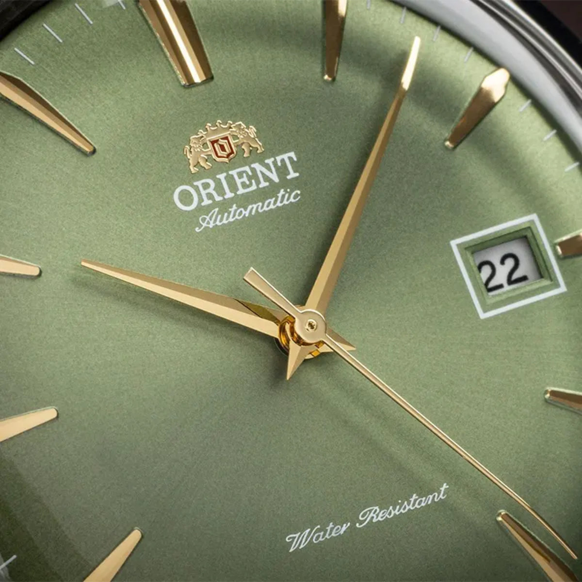 Close-up of Orient Bambino RA-AC0P01E30B showing green dial texture, date display window, and gold-tone hands