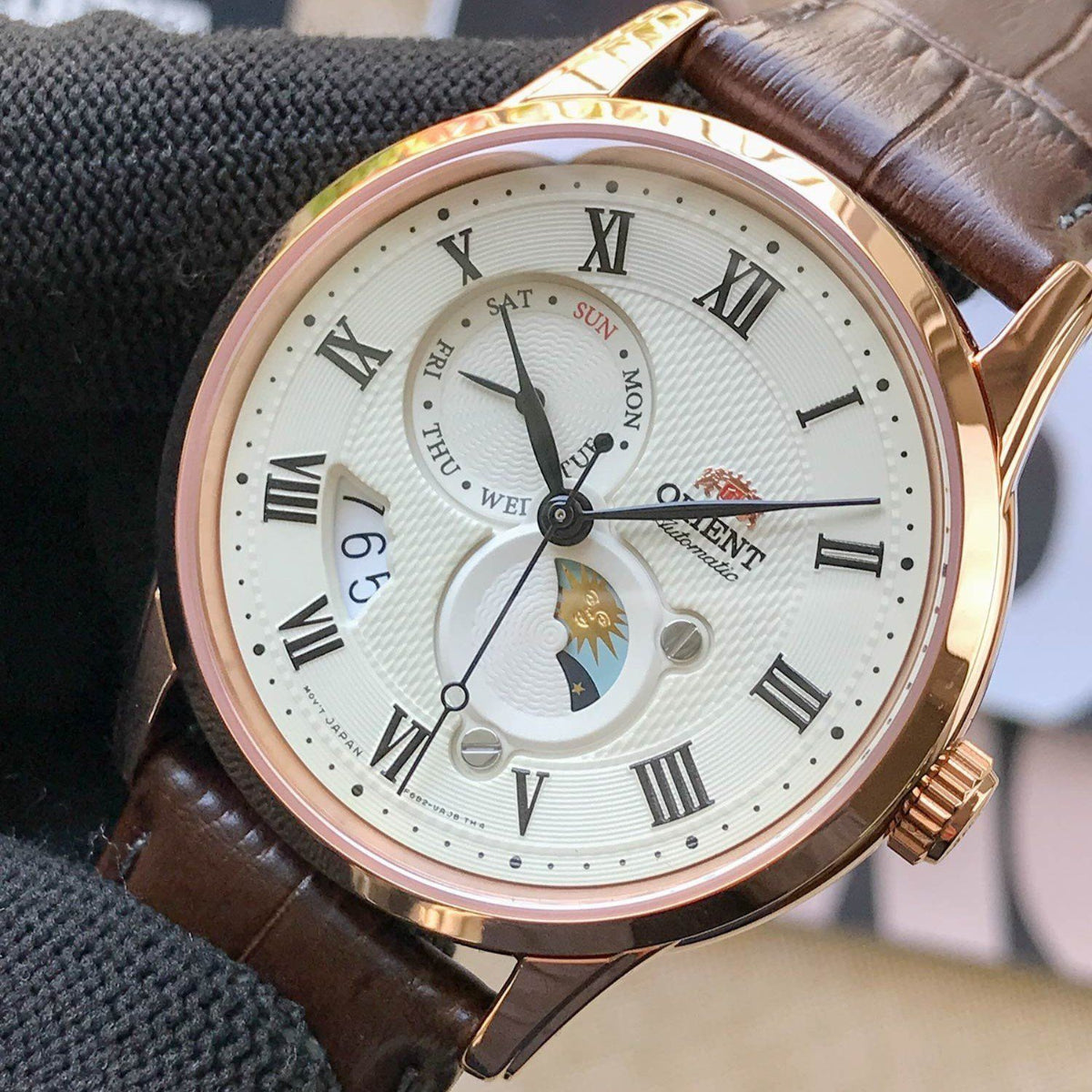 Orient Bambino Sun & Moon RA-AK0007S30B mens mechanical wrist watch held with gloved hand showing champagne dial and rose gold case