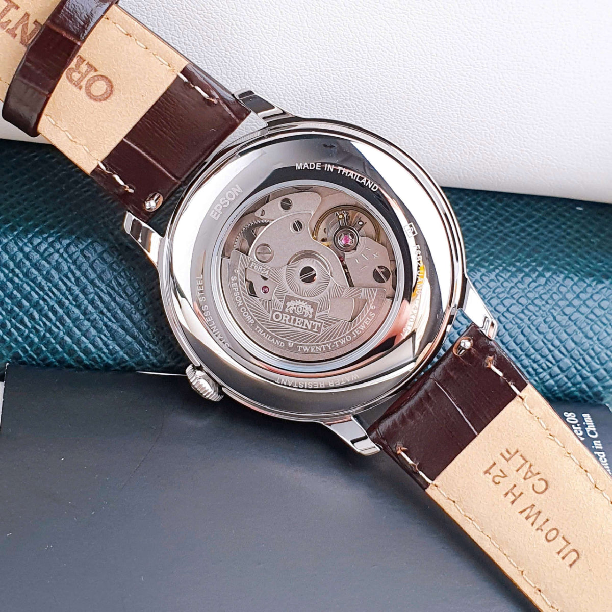 Close-up view of exhibition case back on Orient Bambino RA-AK0807R30B mens automatic watch resting on presentation cushion