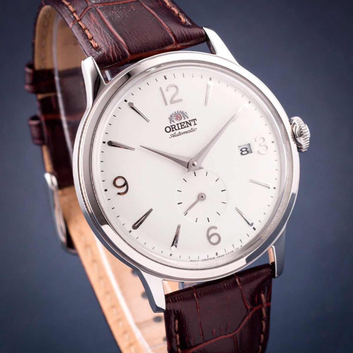 Men's automatic watch close-up: white dial, brown leather strap, crown at right