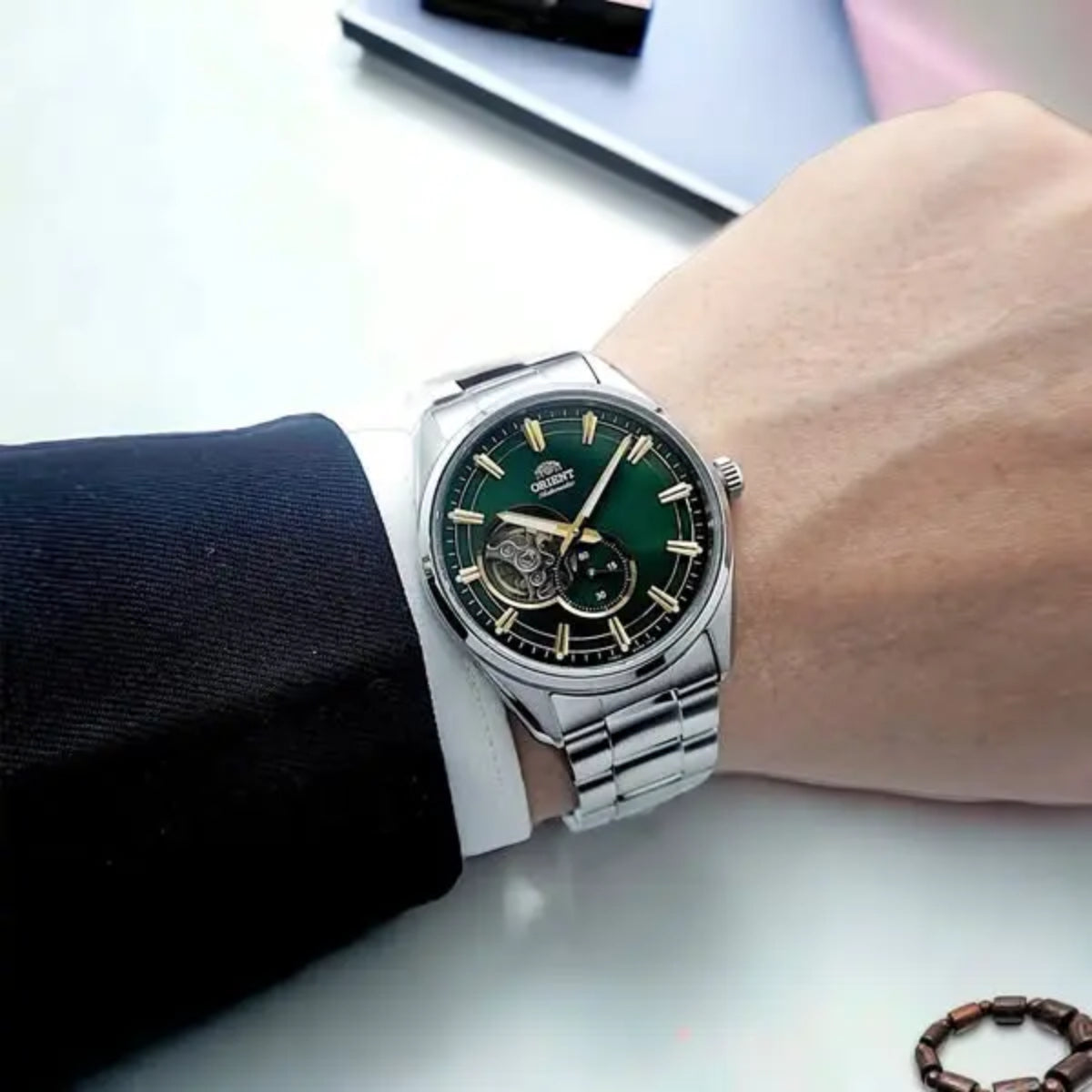 A person wearing the Orient Stretto 41mm Semi Skeleton green dial steel mens automatic watch paired with a black suit jacket sleeve
