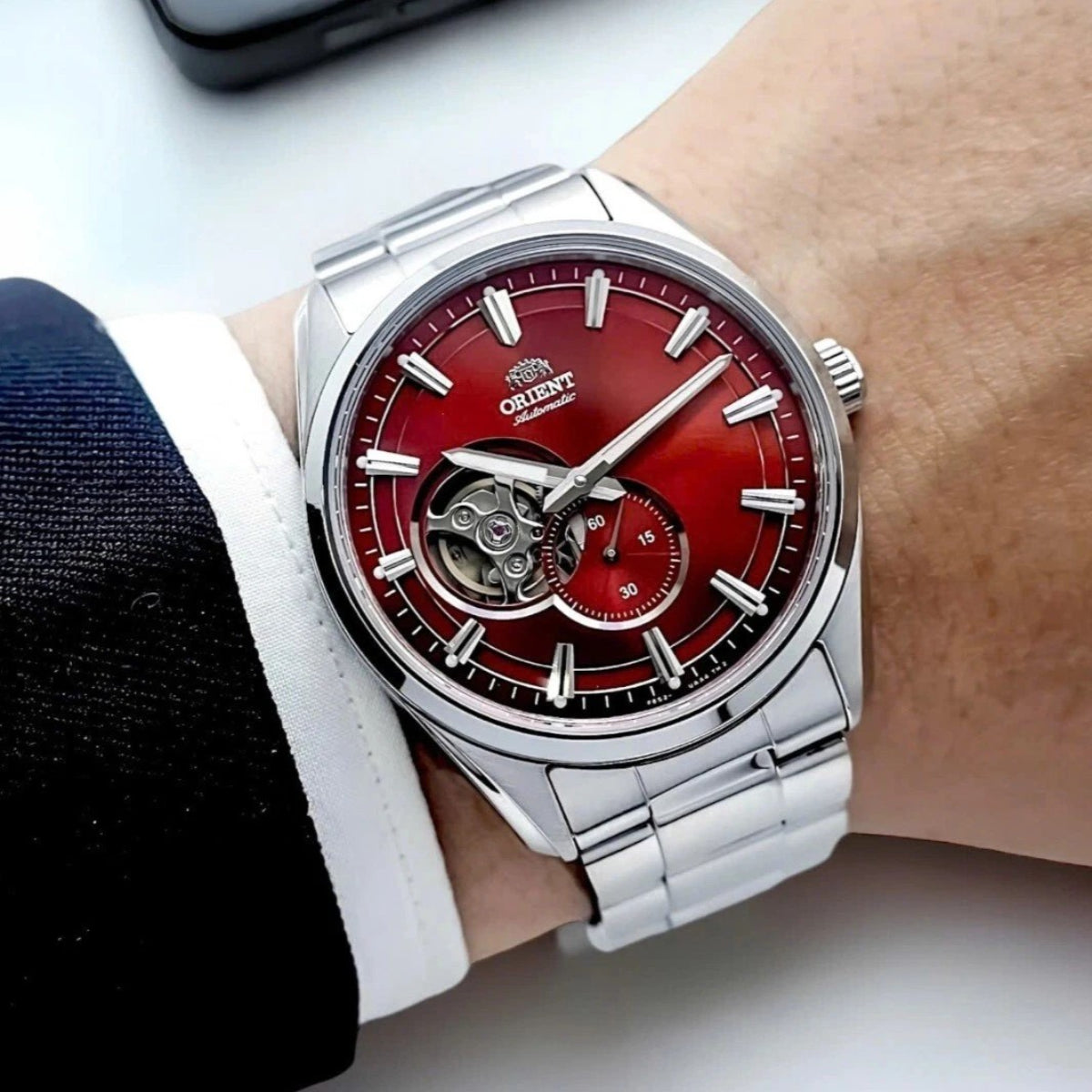 Men's automatic open-heart steel wristwatch on wrist with red dial and skeleton window