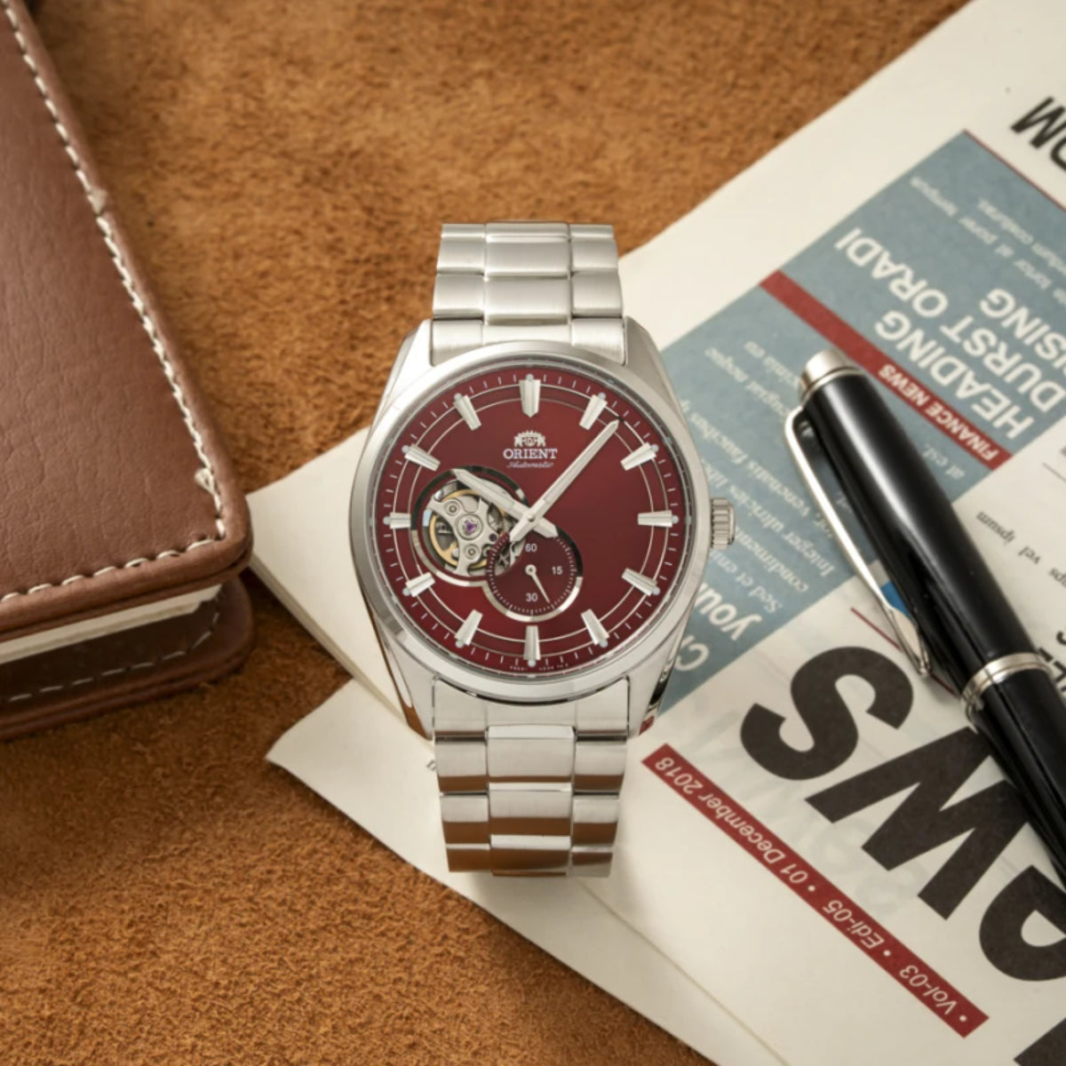 Men’s steel automatic watch with red dial on leather surface with booklet