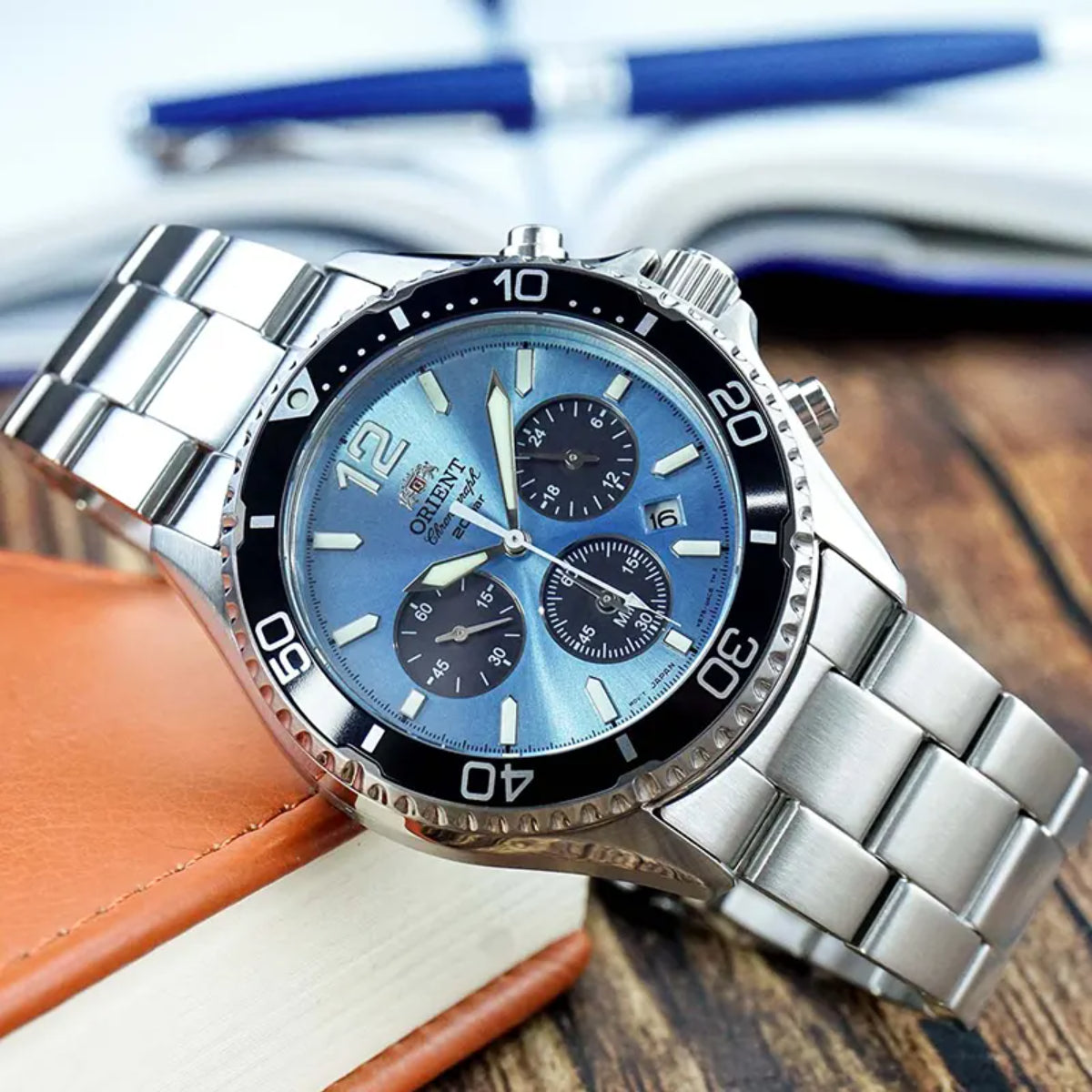 Stainless steel chronograph watch with blue dial and black bezel on brown leather surface.