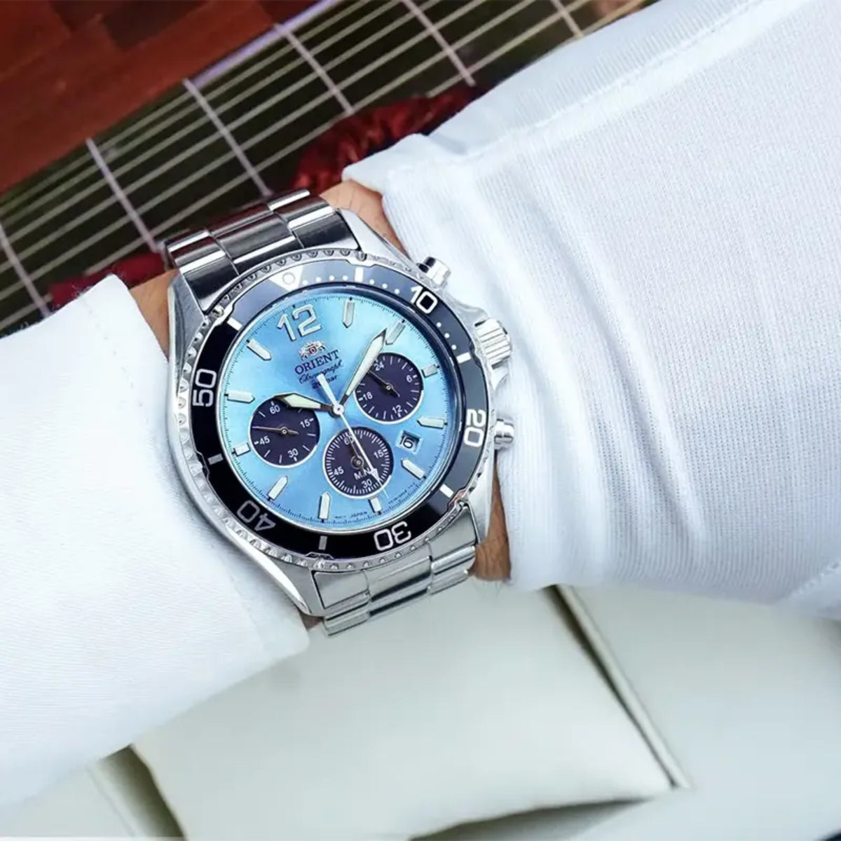 Men's wristwatch with blue chronograph dial and stainless steel bracelet on white sleeve.