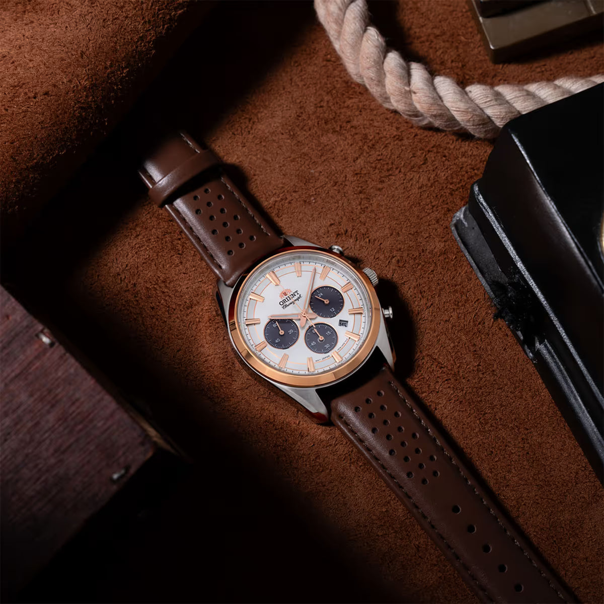 Solar chronograph watch with brown perforated leather strap lying on leather surface