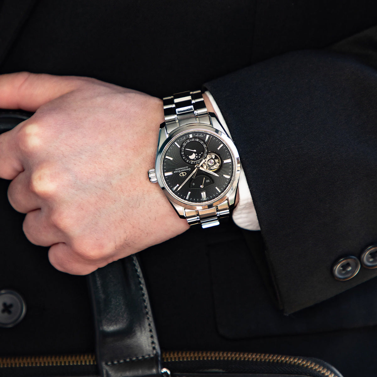 Men's wrist watch with steel bracelet and black dial, worn with suit sleeve